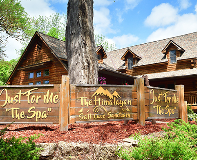 outdoor wooden sign reading "Just For Me The Spa" and "The Himalayan Salt Cave Sanctuary" in yellow lettering