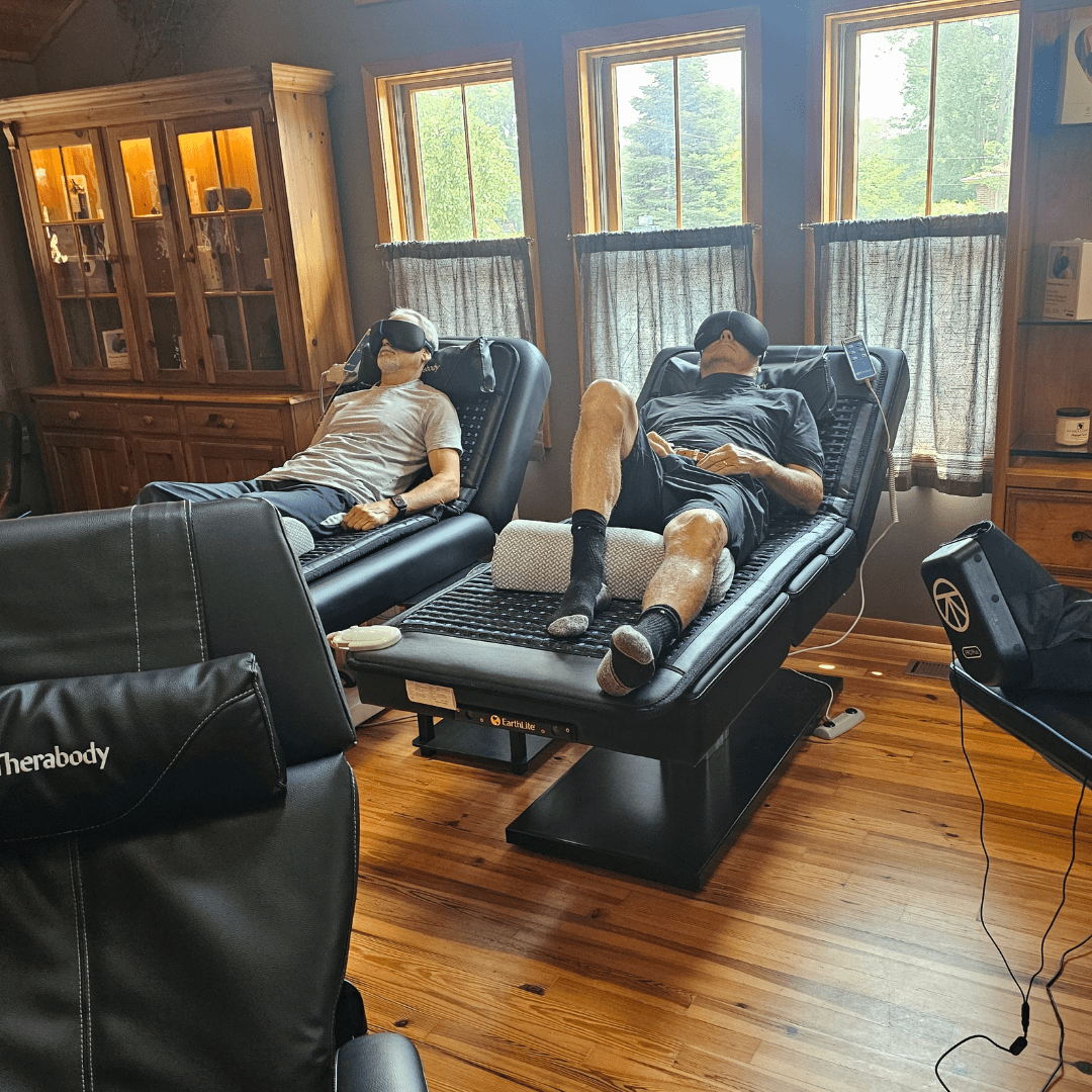2 individuals laying on PEMF Grounding Mats and using TheraFace Mask or SmartGoggles