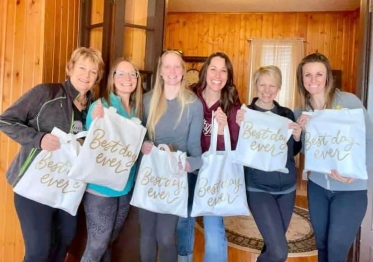 group of women smiling and holding white bags that read "best day ever"