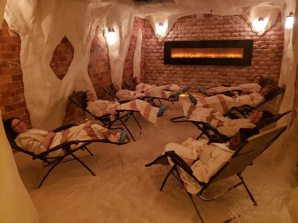 group of people smiling in chairs in salt cave with blankets on