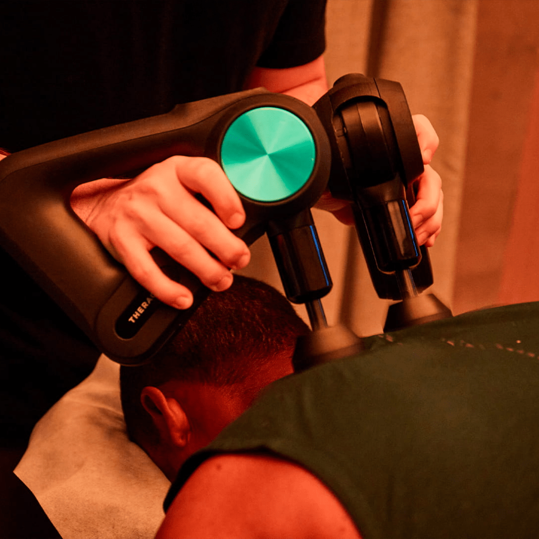 man receiving Theragun percussion massage on shoulders