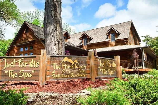 outdoor wooden sign reading "Just For Me The Spa" and "The Himalayan Salt Cave Sanctuary" in yellow lettering