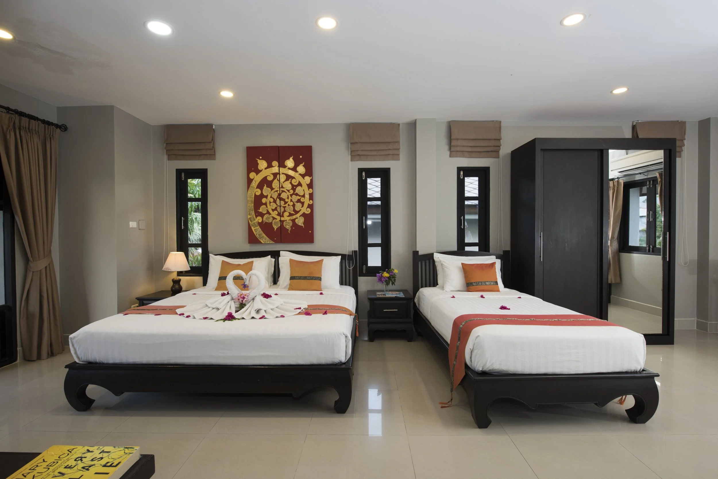 Hotel room with two beds, decorated with towel swans and flowers, a lamp, artwork above the beds, and a closet with a mirror door.