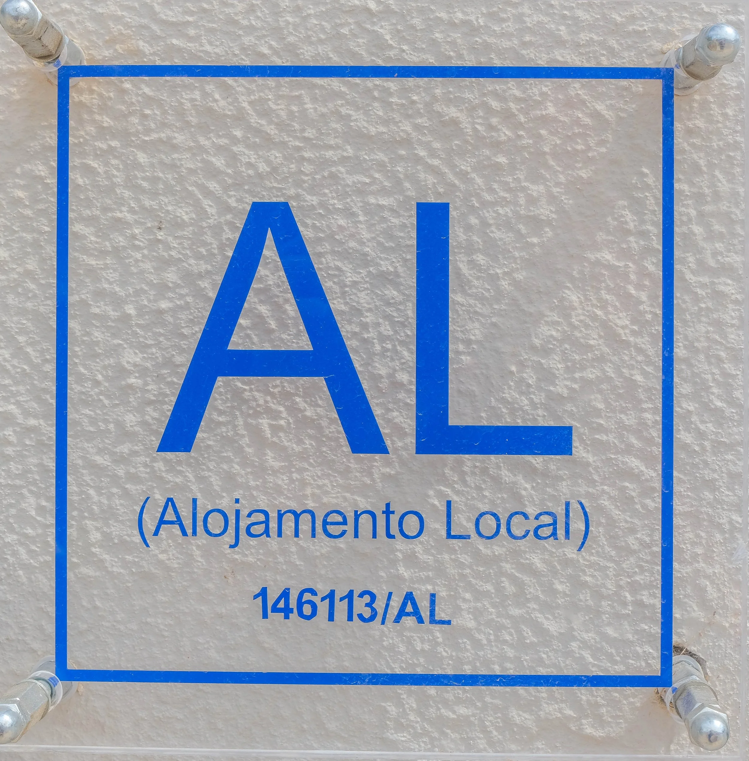 Sign with blue text indicating 'AL (Alojamiento Local) 146113/AL' on a textured white wall.