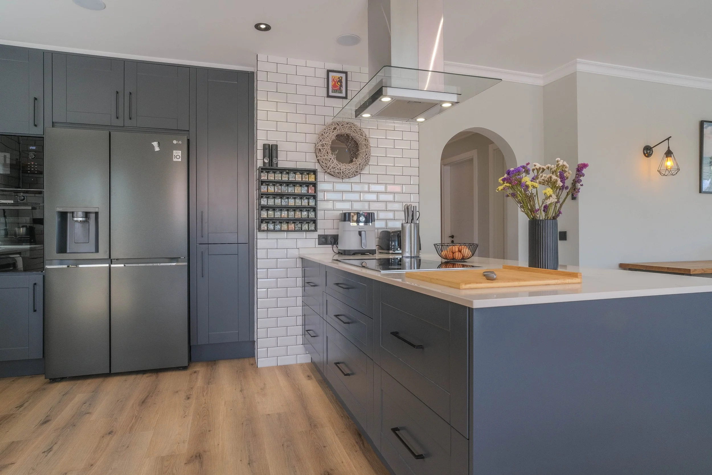 Modern kitchen with gray cabinets, a double-door refrigerator, white subway tile backsplash, wooden flooring, and kitchen appliances on the counter.