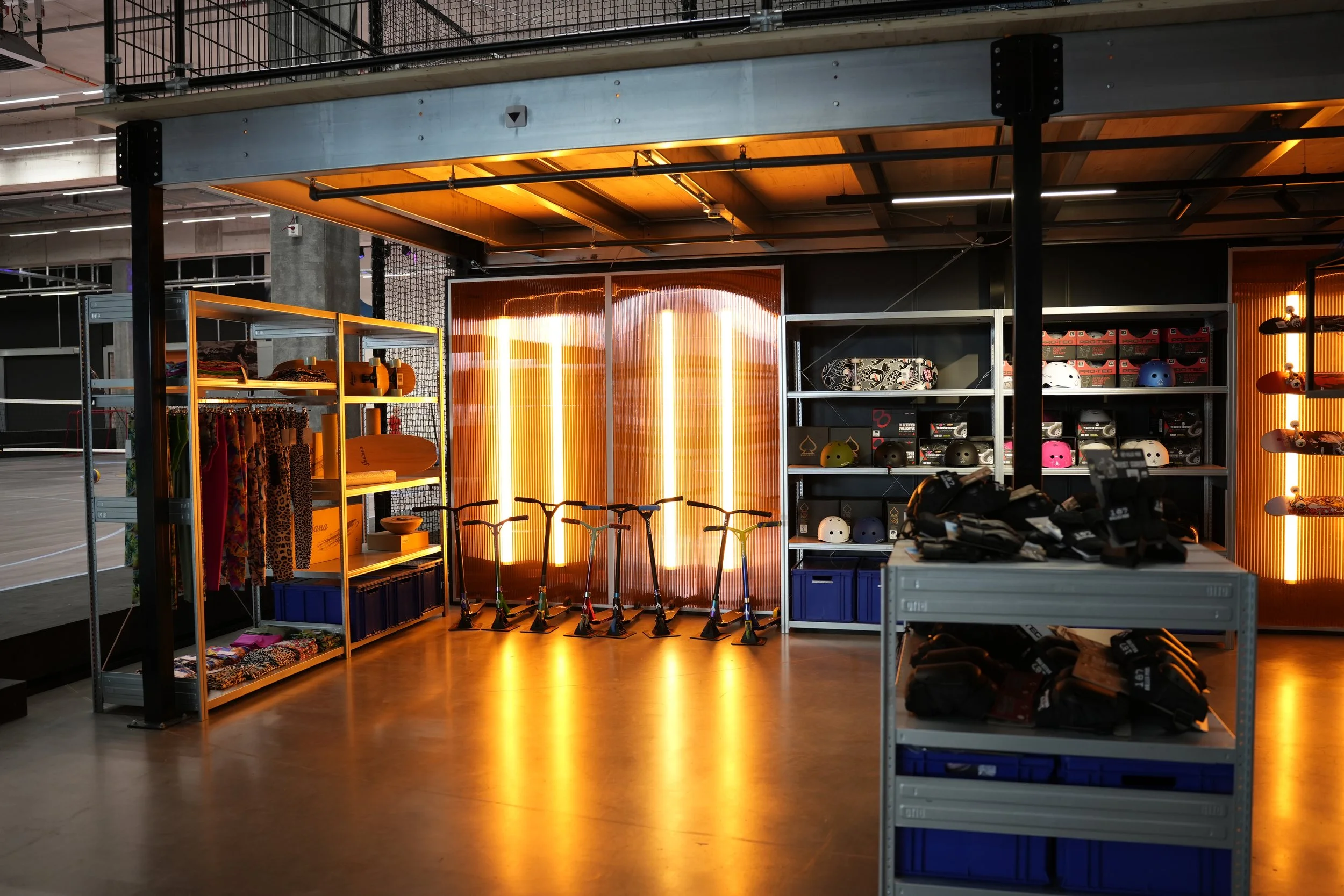 Ein Indoorsportgeschäft mit Helmen, Scooter, Skateboards und Zubehör auf Regalen, beleuchtet mit warmem Licht.