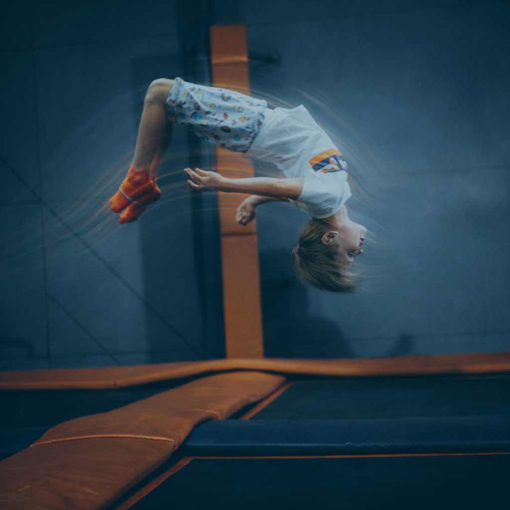 Ein Kind springt rückwärts auf einem Trampolin mit blauer Wand im Hintergrund.
