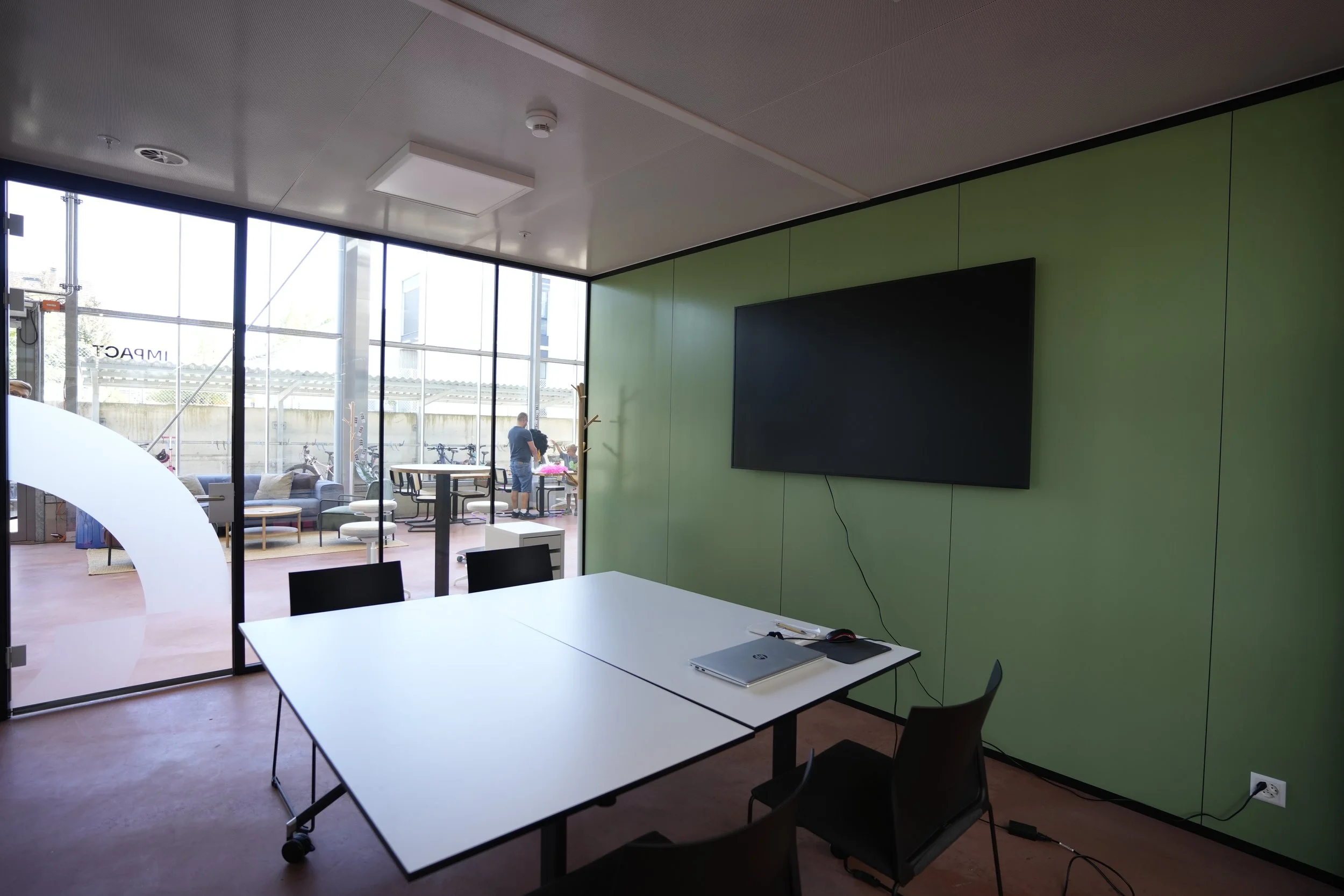 Moderner Konferenzraum mit weißem Tisch, weißen Stühlen auf Rollen, Wandpaneelen aus Holz, TV an der Holzwand, blauer akustischer Decke mit modernen Lichterleuchten.