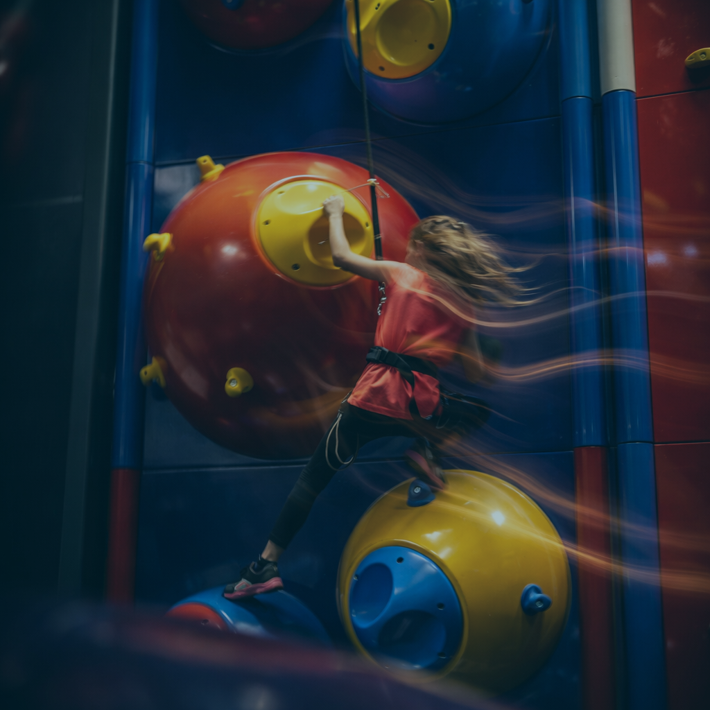 Ein Mädchen beim Klettern an einer Indoor-Kletterwand, die mit großen bunten kugelförmigen Kletterelementen ausgestattet ist.