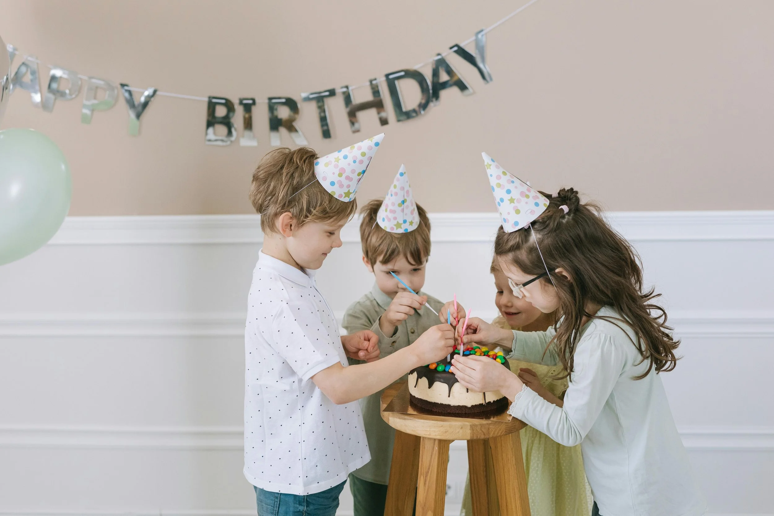 Vier Kinder feiern Geburtstag mit Kuchen und Partyhüten, im Hintergrund ein 'Happy Birthday'-Banner.