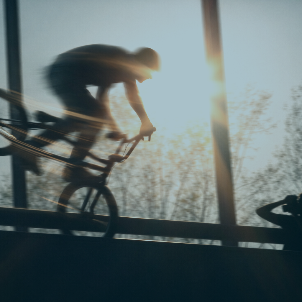 Ein Fahrradfahrer in Bewegung bei Sonnenlicht, im Hintergrund sind Bäume und eine klare Himmelsszene.