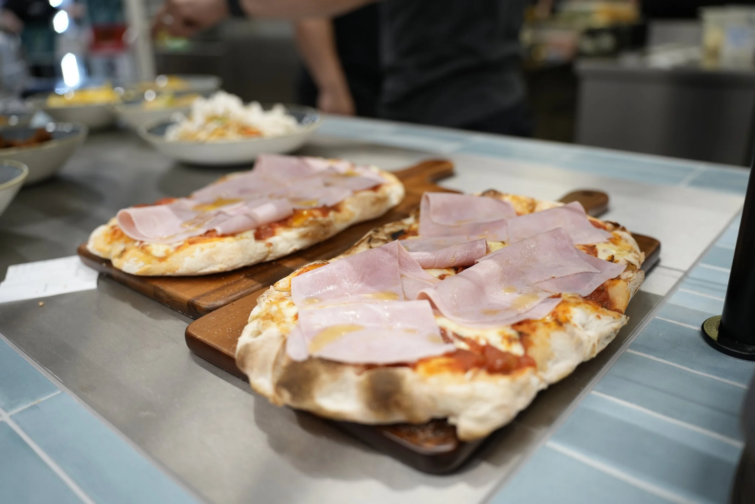 Vier Pizzastücke mit Schinken auf Holzplatten auf einem Tisch.