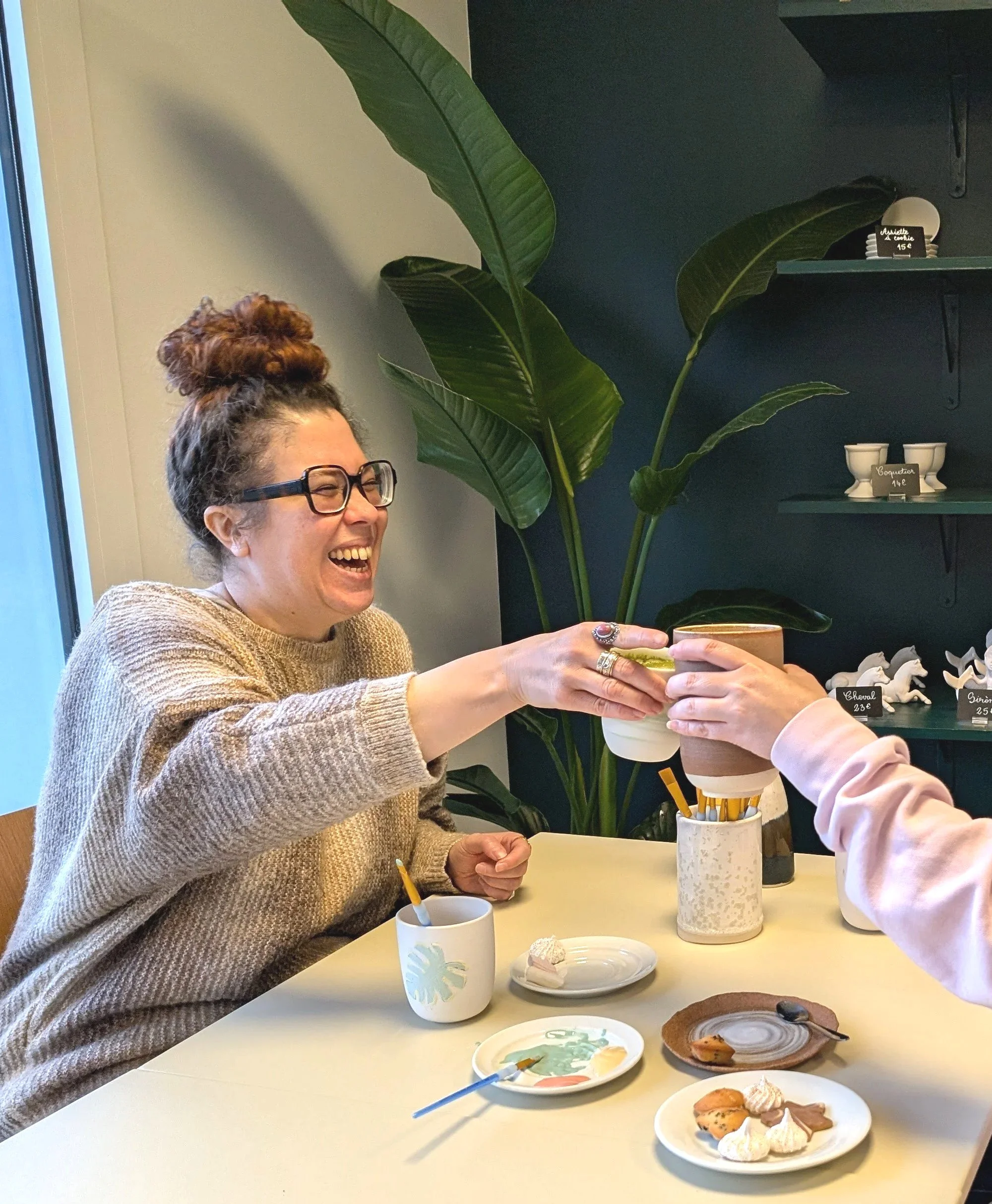 Deux amies échangent un café dans le café céramique Décore-moi à Labenne, avec des desserts sur la table, environment convivial et cosy avec des plantes en arrière-plan.