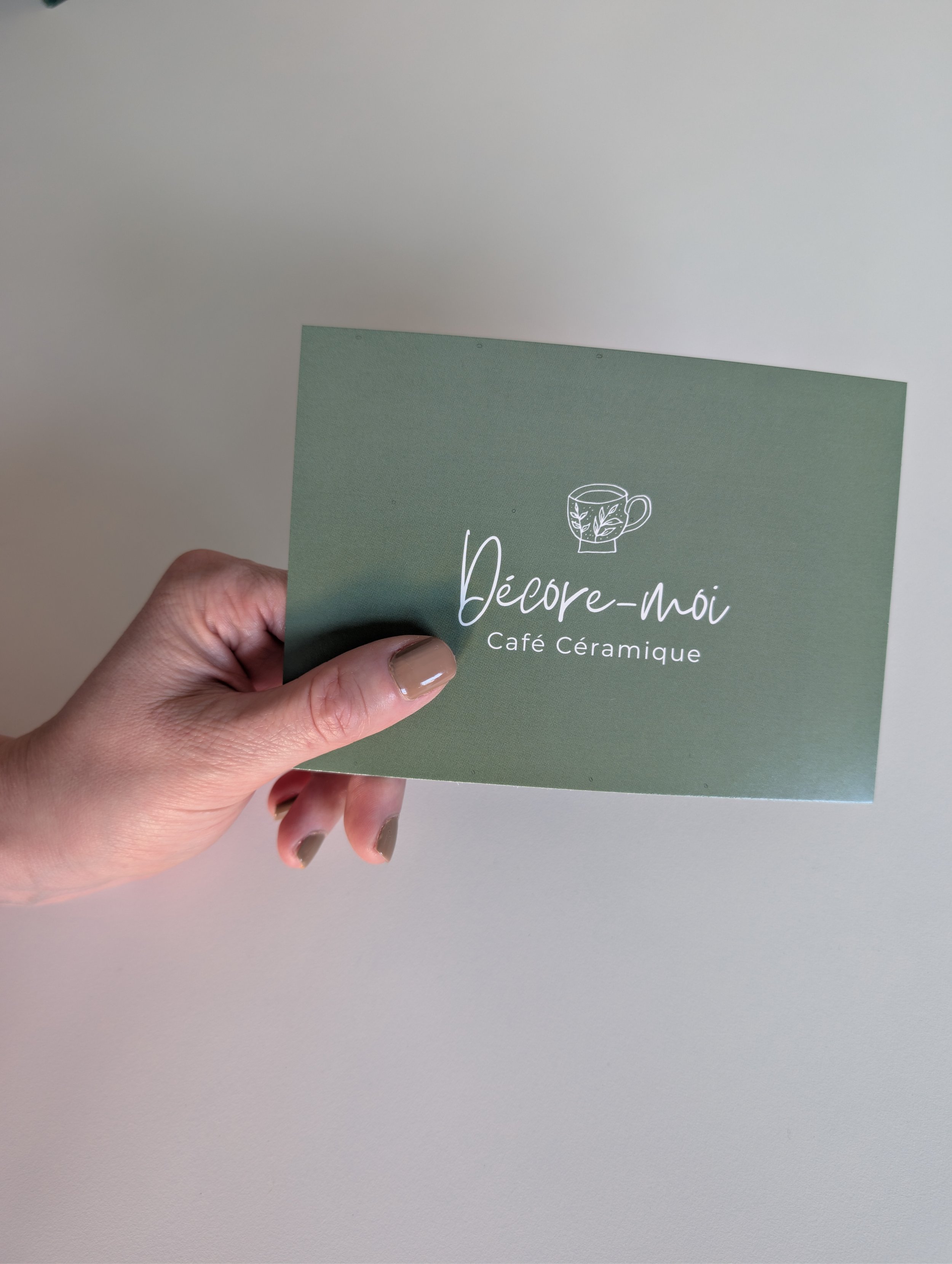 Une main tient une carte cadeau avec le texte 'Décore-moi Café Céramique' et le logo du café céramique.