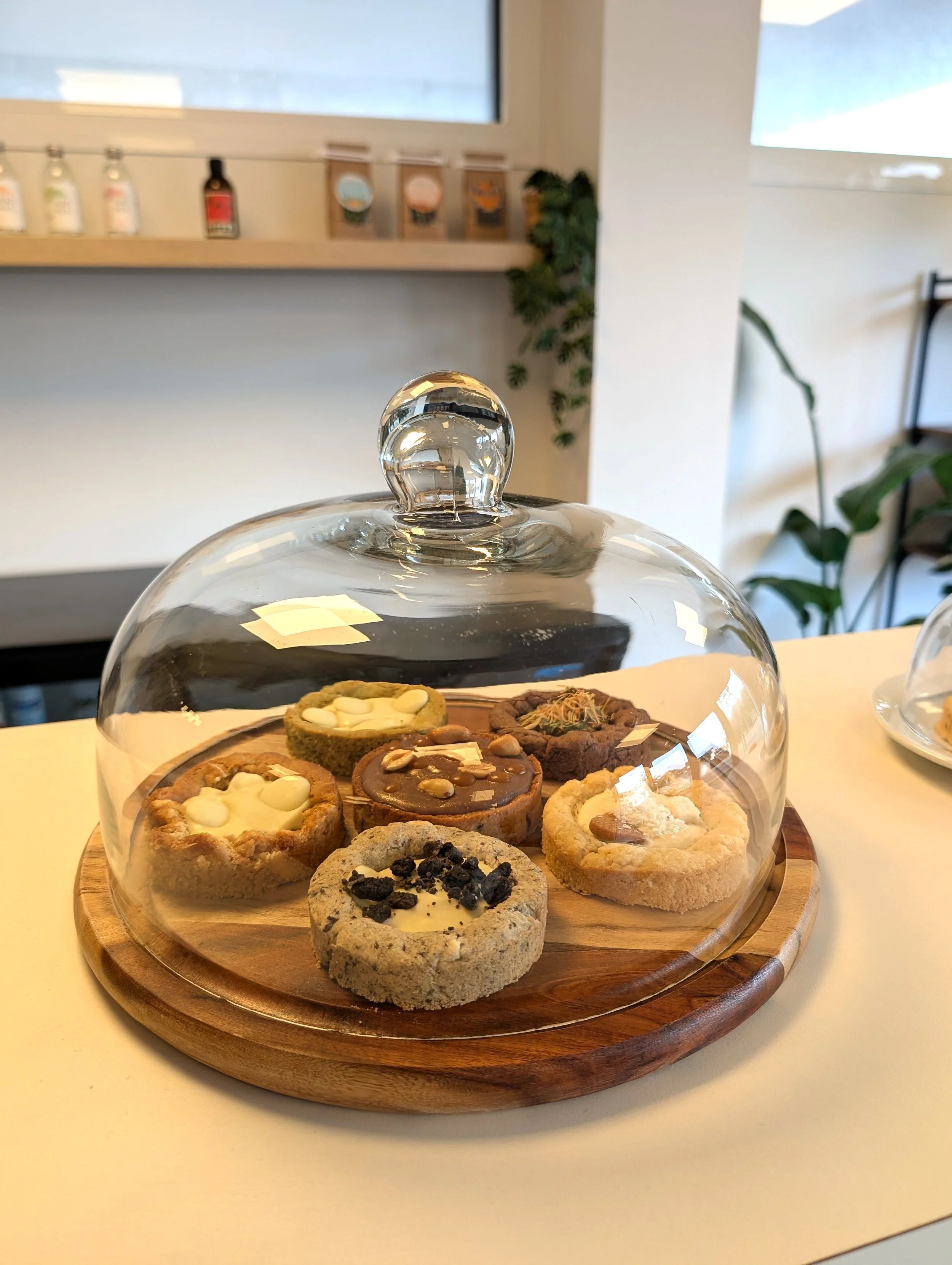 Plateau de cookies variés sous une cloche en verre sur une planche en bois, pâtisseries réalisées par L'Univers de Christelle 40.