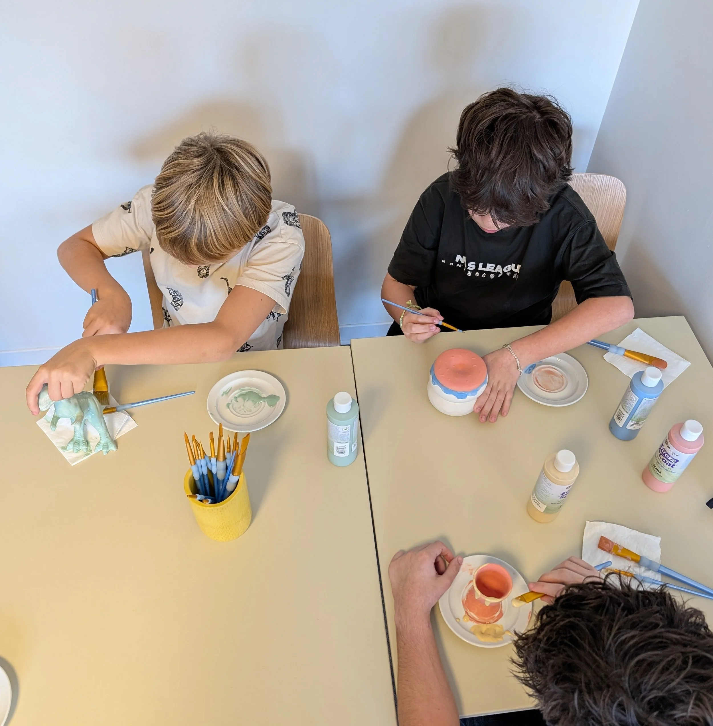 Trois enfants qui peignent des objets en céramique dans le café céramique Décore-moi à Labenne, moment de détente et de créativité entre amis.