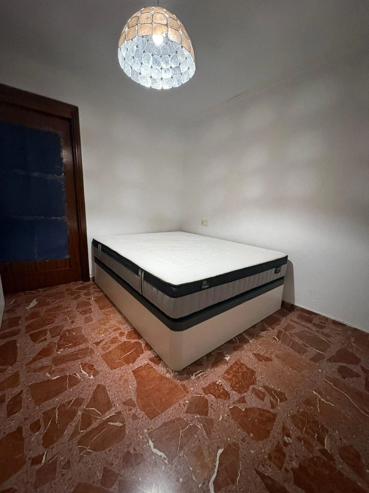 Habitación vacía con cama doble, puerta de madera con cristal y lámpara en el techo