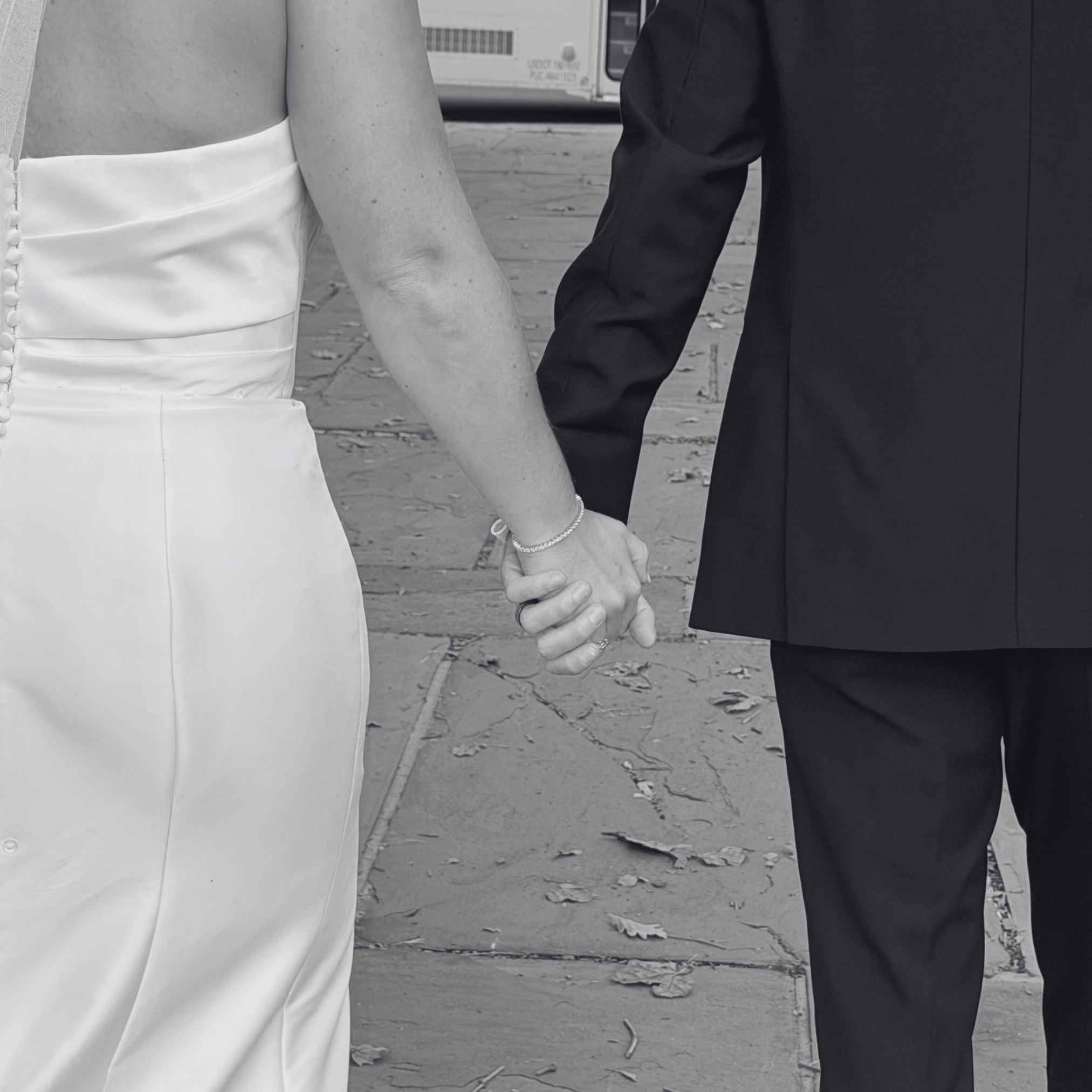 A bride and groom holding hands during their wedding, with the bride wearing a white satin gown and the groom in a black suit.