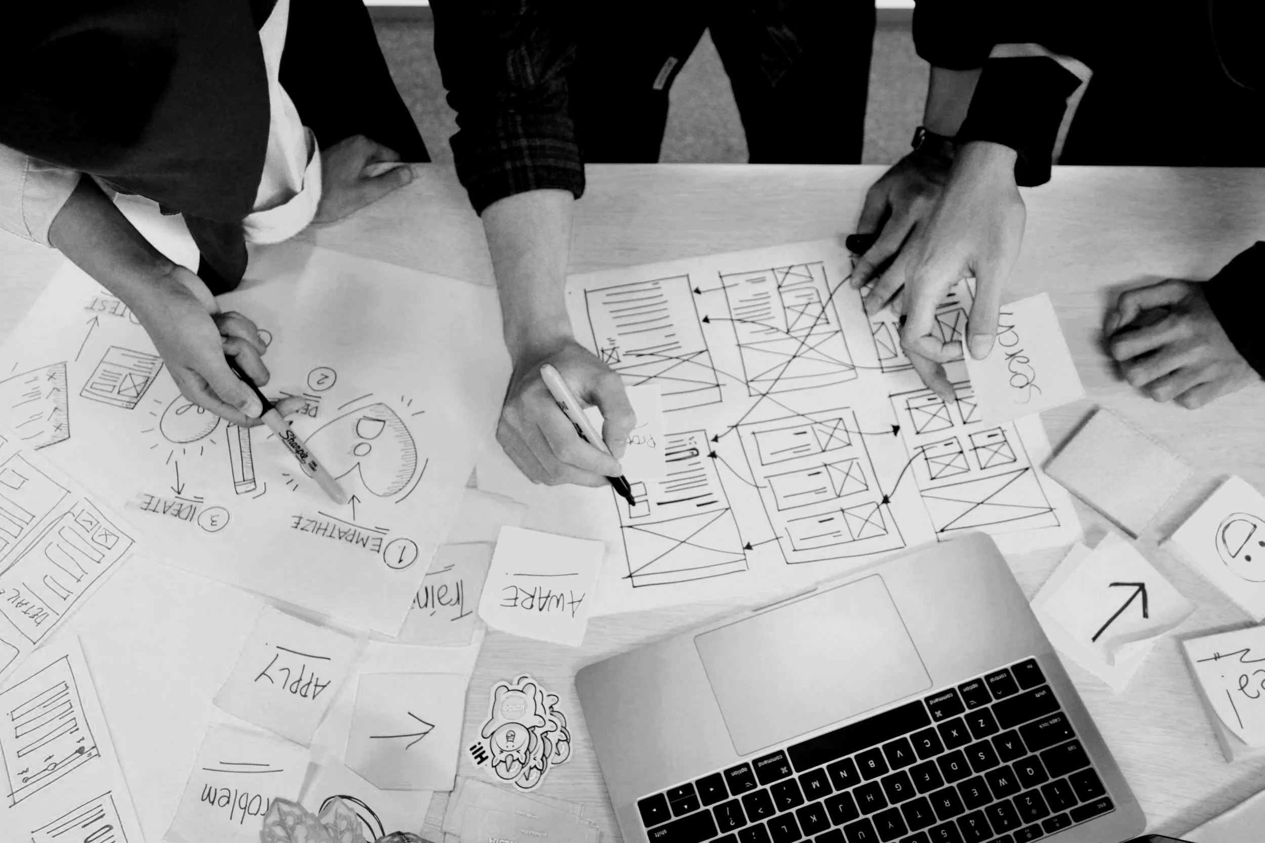 Groupe de personnes travaillant sur un tableau de wireframes pour un projet, avec des notes et des croquis distribués sur toute la table pendant une séance de brainstorming.