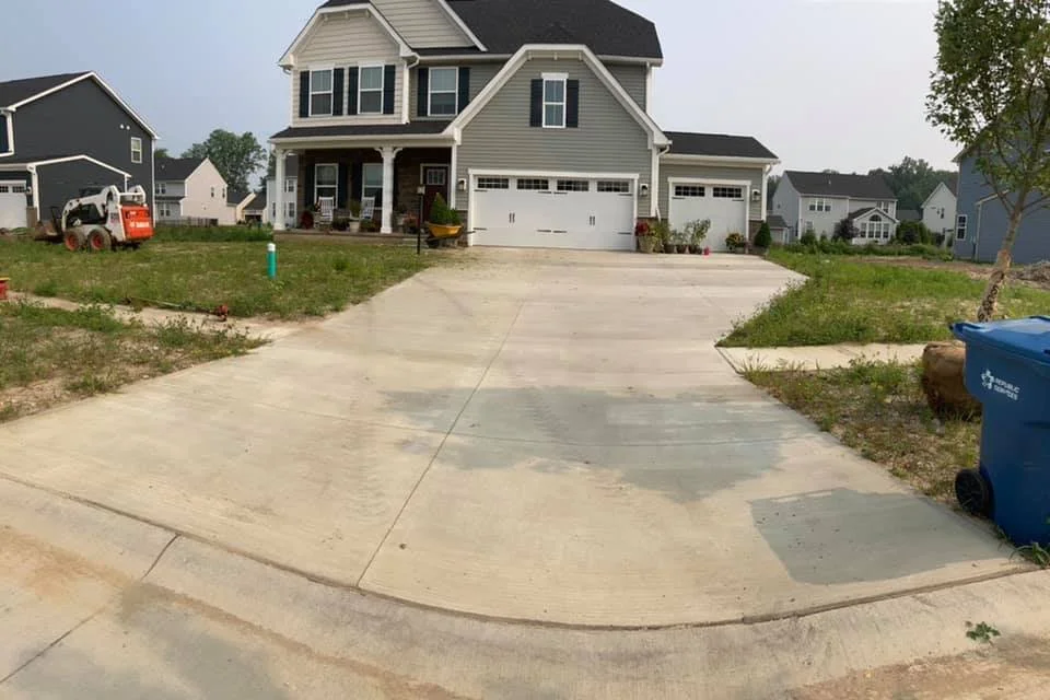 A new, two-story suburban house with a large front driveway, a garage, and a porch, situated in a neighborhood with other similar houses.