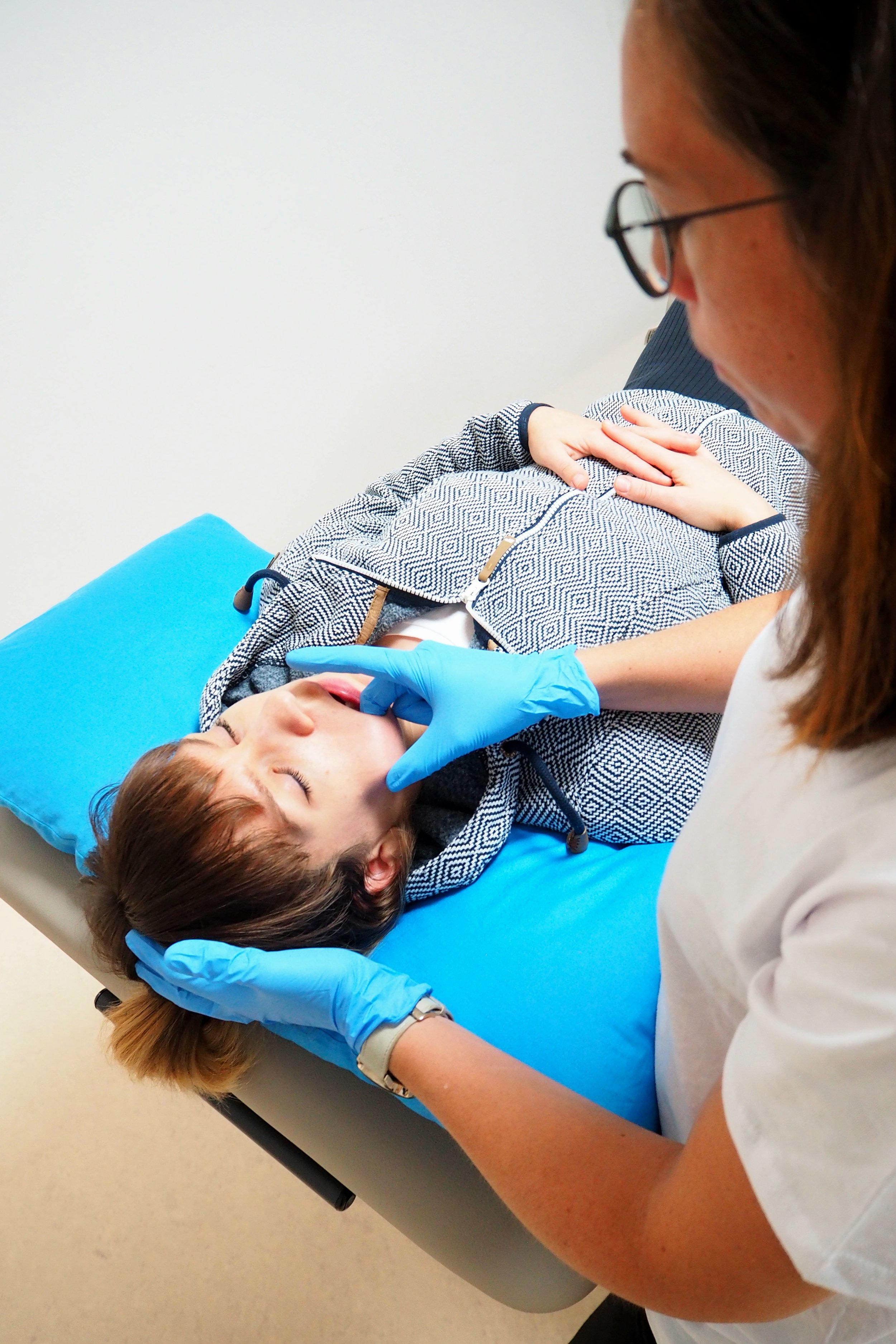 Eine Frau mit blauer Handschuhen behandelt einen Patienten, der auf einer Untersuchungsliege liegt, am Kiefer. Sabine Wieser Physiotherapeutin