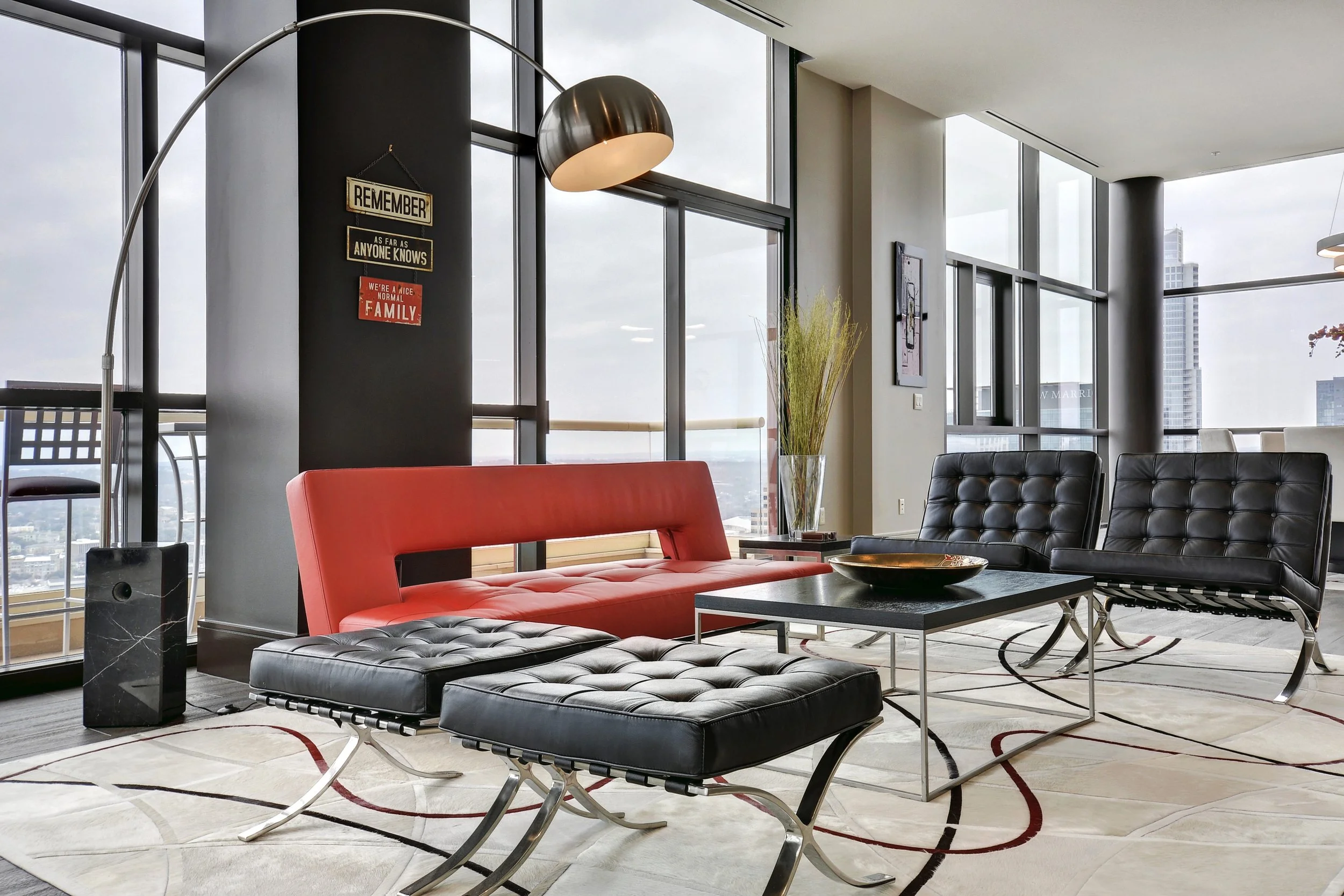 Modern living room with large windows, black and red seating, a coffee table, and a tall floor lamp