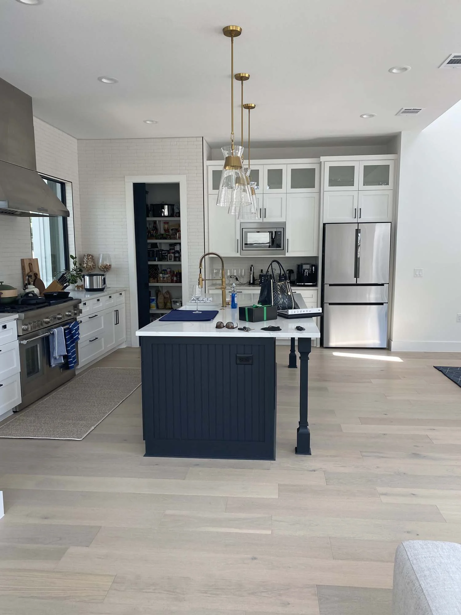 Modern kitchen with white cabinets, a black island, stainless steel appliances, and a light wood floor. Hanging glass light fixtures above the island.