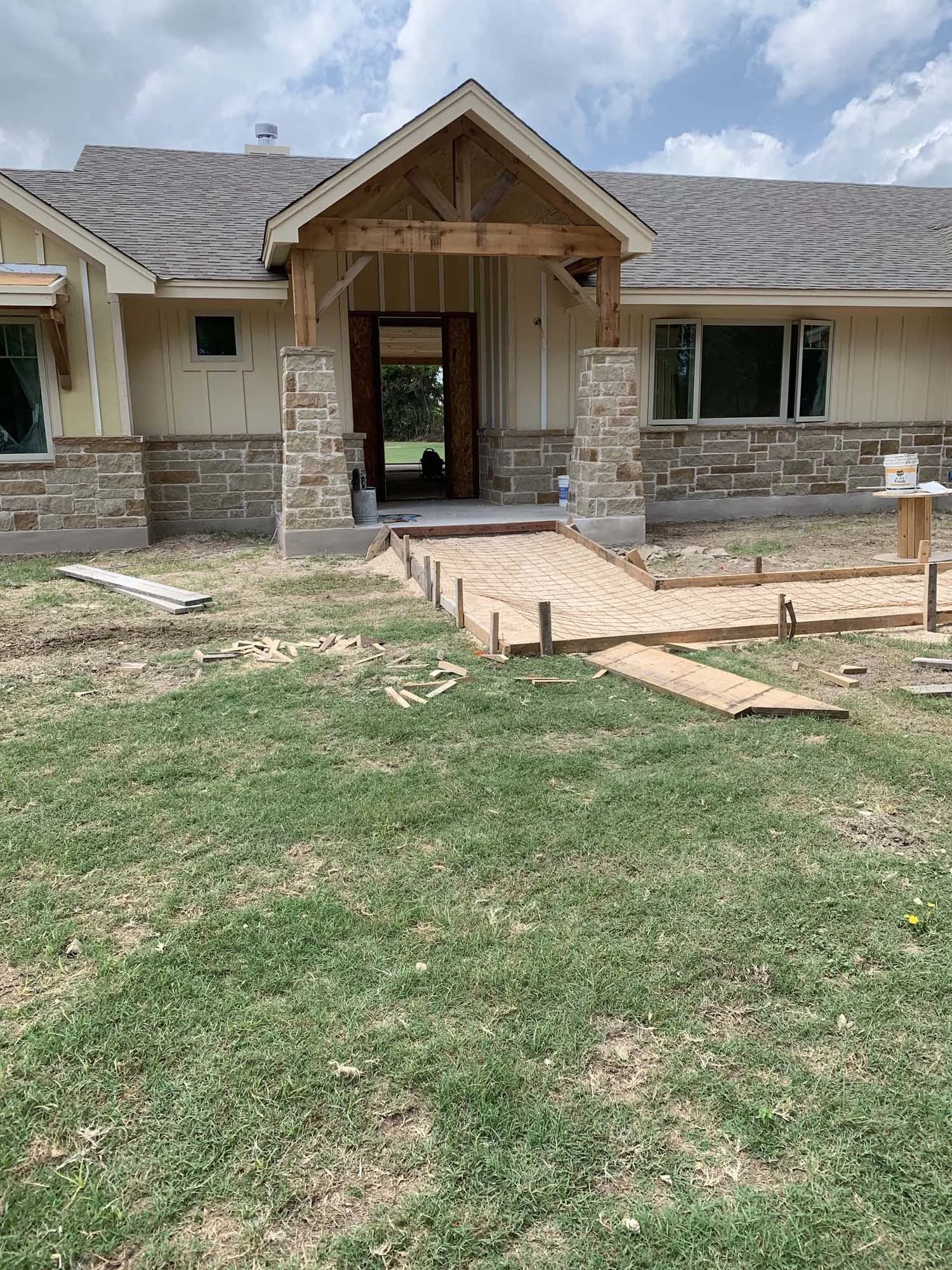 Under-construction house entrance with brick and wood framing, construction materials, and a partially finished pathway leading to the front door.