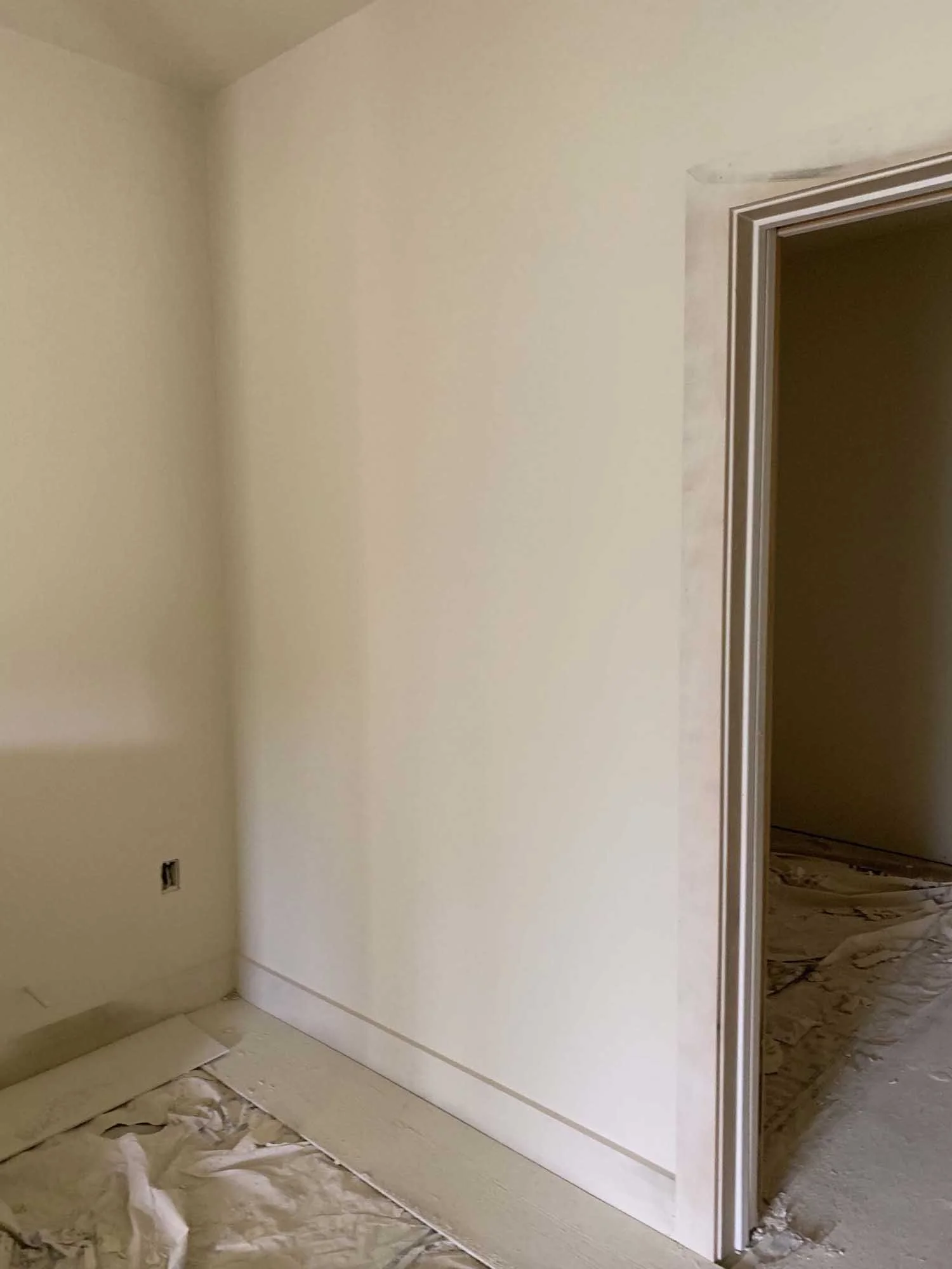 Close-up of a newly painted cream-colored wall and doorway in a room under construction, with protective paper on the floor.
