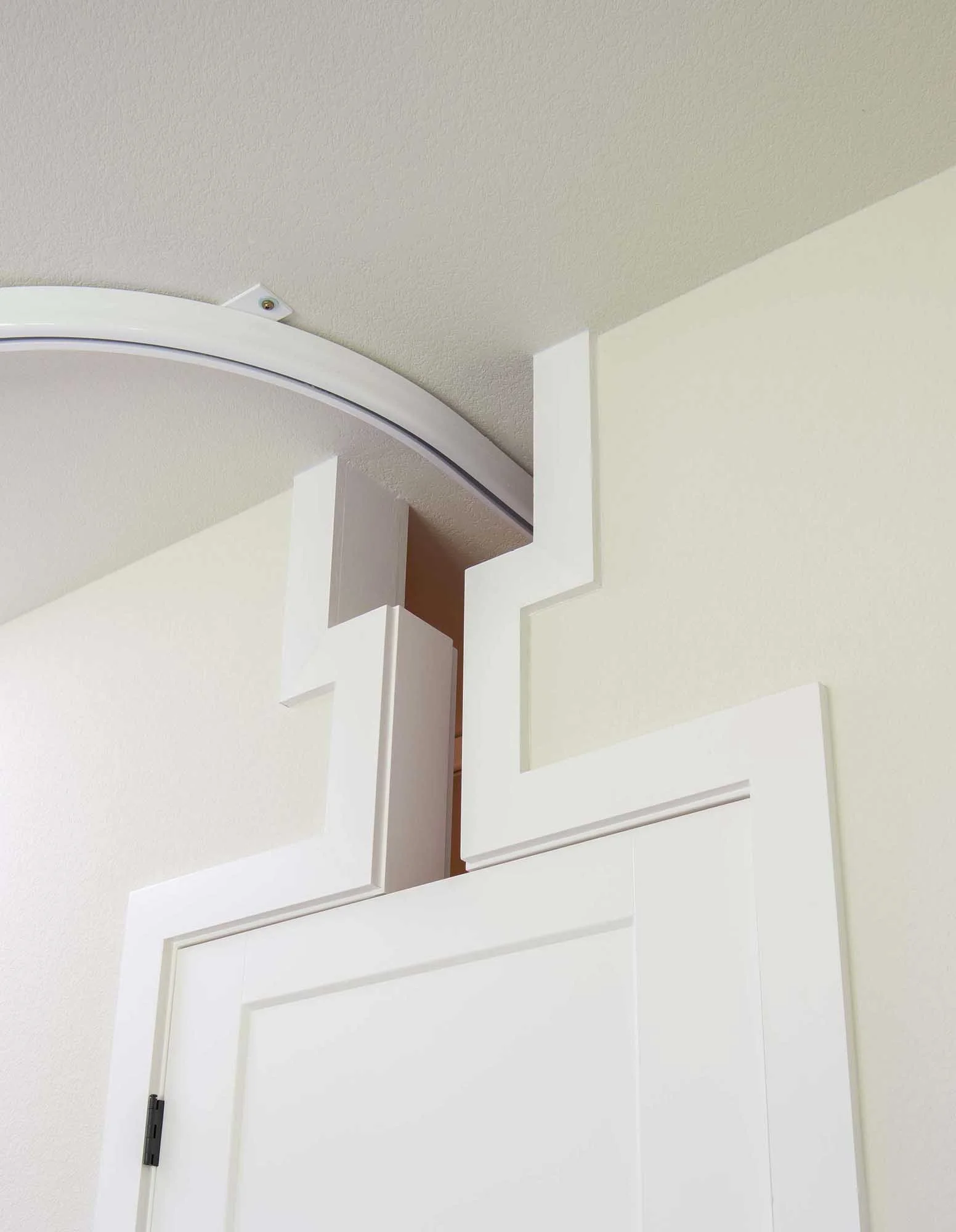 Close-up of a white door with decorative molding and a curved metal rail attached to a ceiling with textured beige paint.