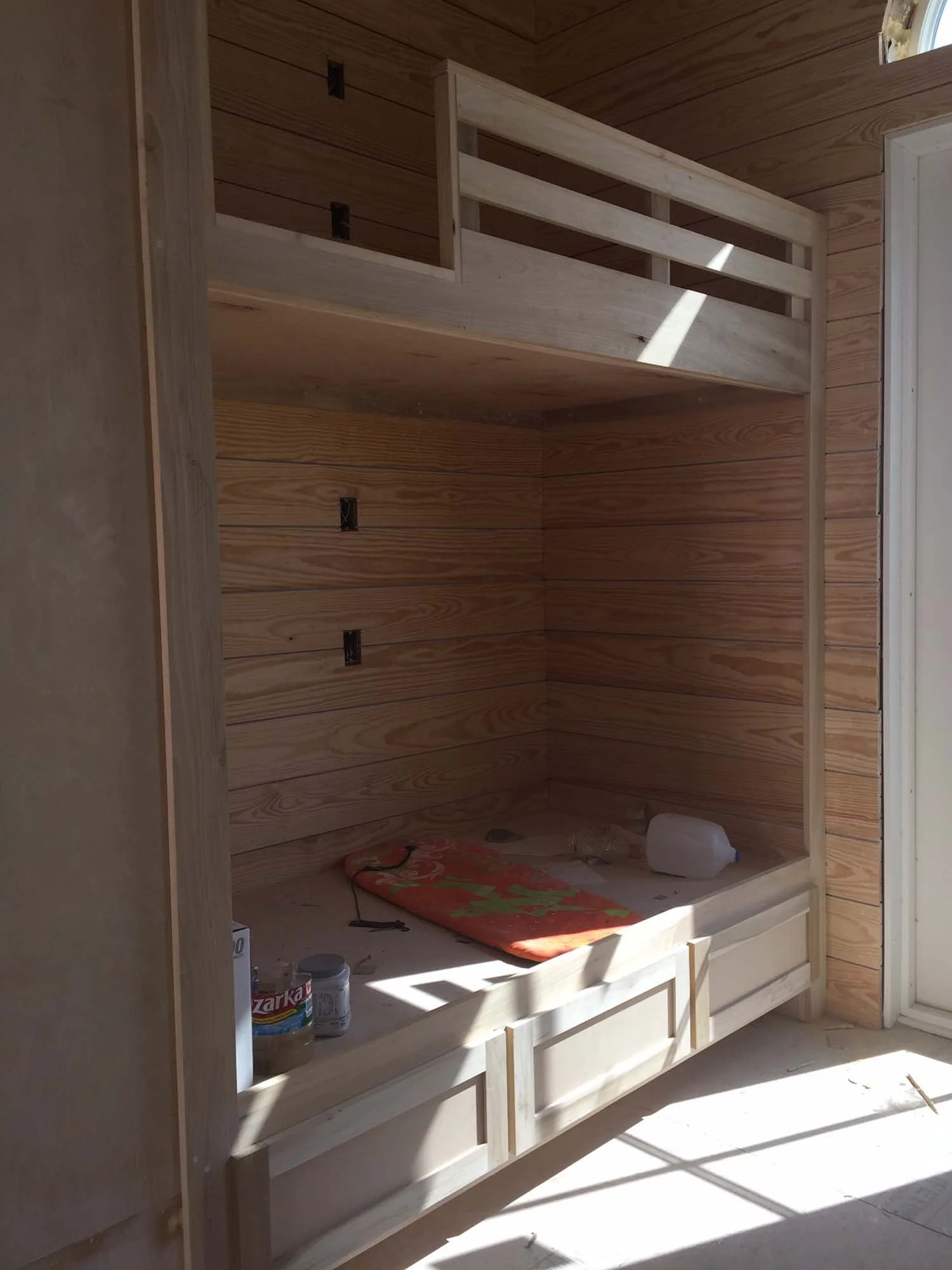 Wooden built-in bunk bed frame inside a room with wood-paneled walls, with some construction tools and items on the lower surface.