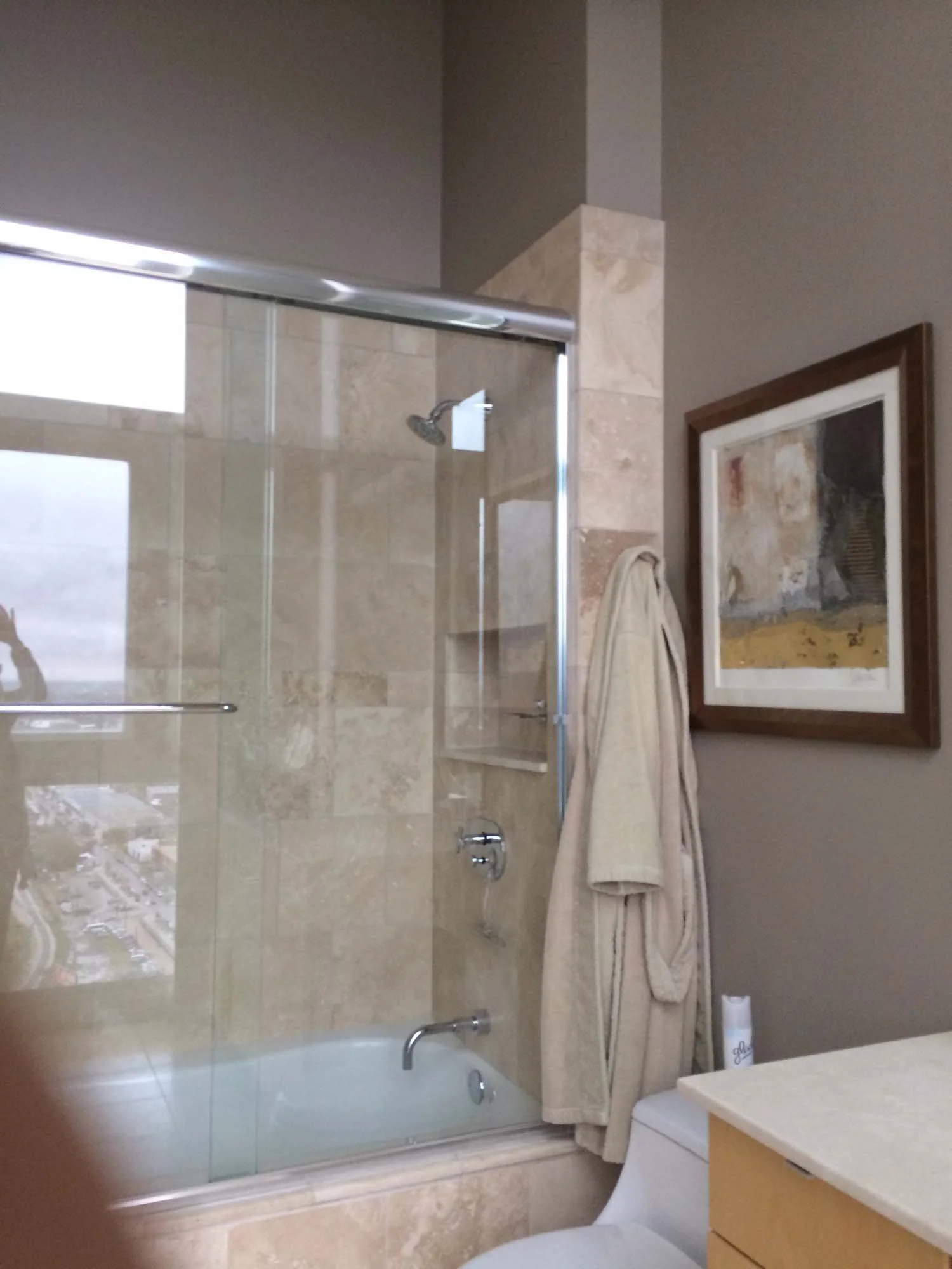 Bathroom with a glass shower enclosure, a bathtub, a towel hanging on the wall, a framed painting, and a toilet.