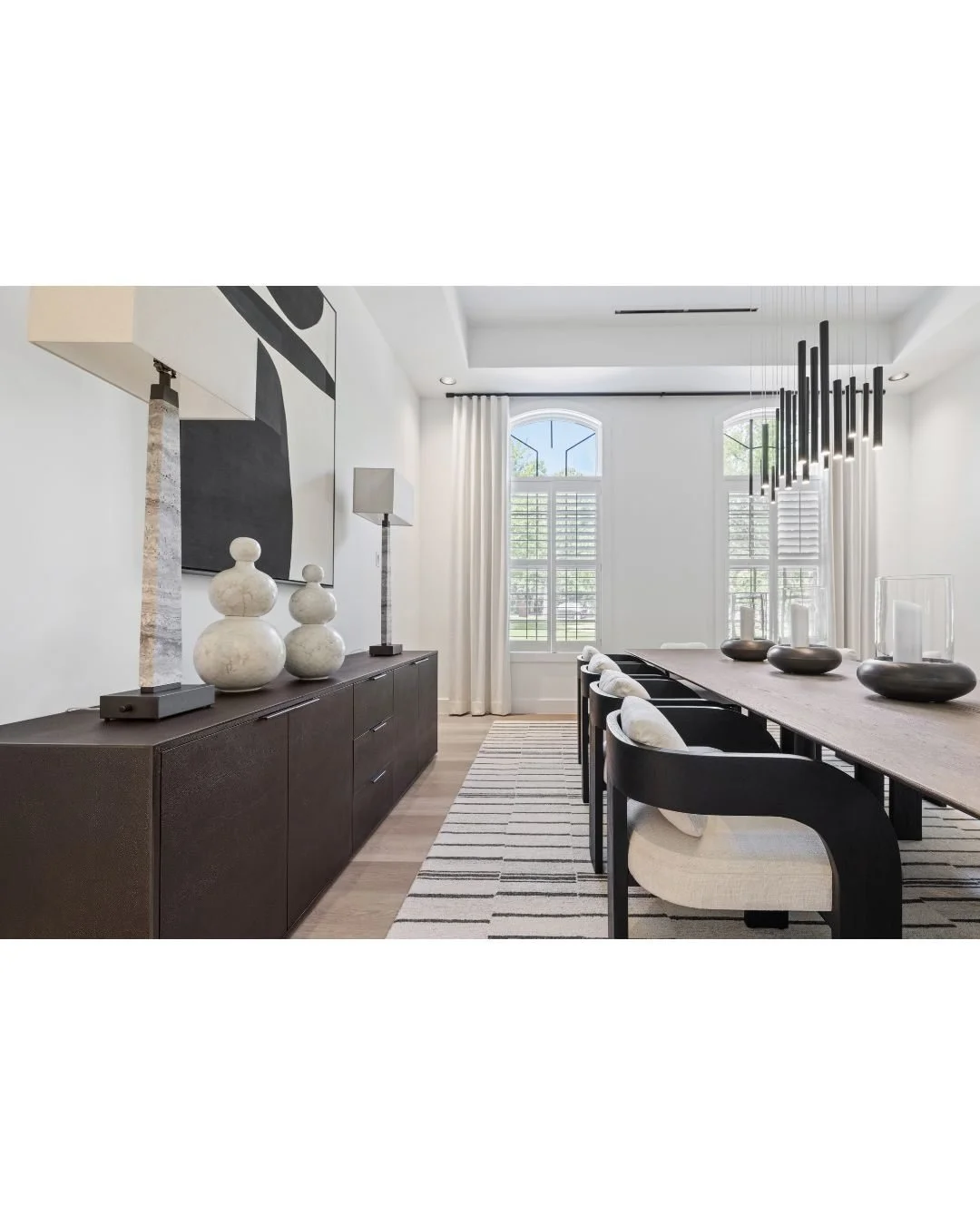 A side angle of the dining room offers a closer look at the graceful lines of the chairs. The hurricanes arranged along the center of the table echo the forms found in the artwork. Extra-tall natural stone lamps make a bold statement and hold their o