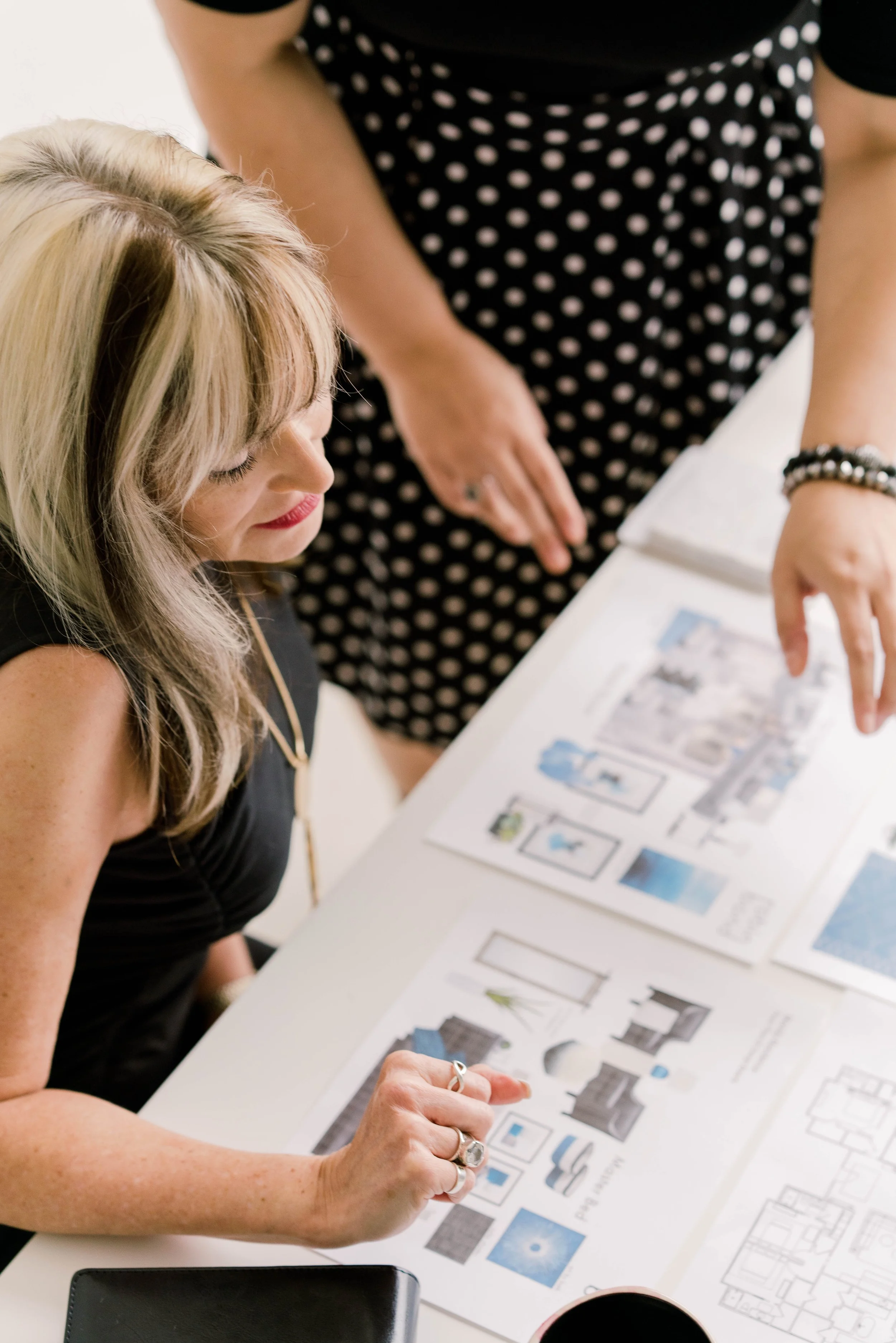 Two women are discussing architectural plans and design ideas laid out on a white table.