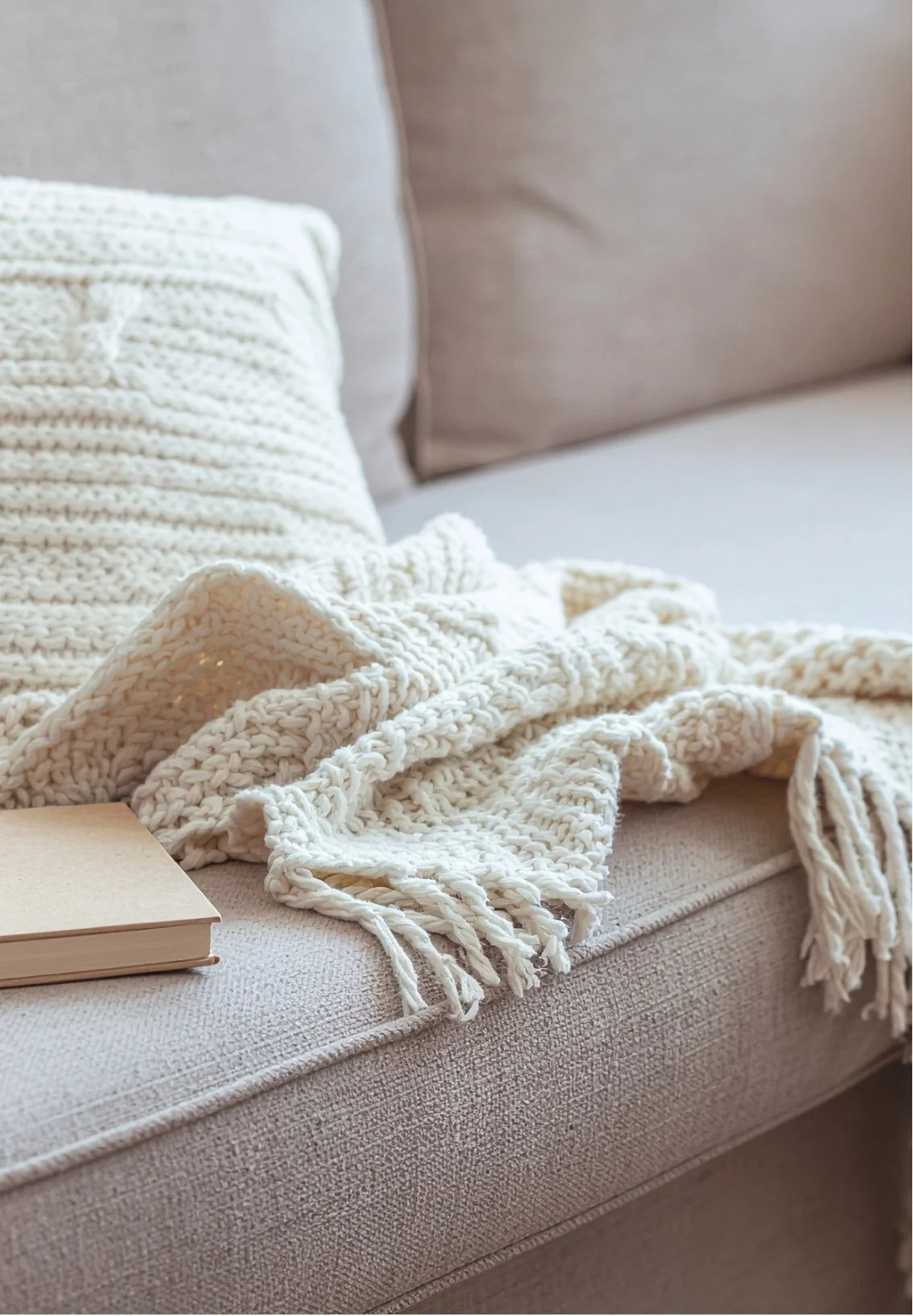 Cozy beige sofa with cream-colored throw blanket and matching pillow, a closed book resting on the sofa.