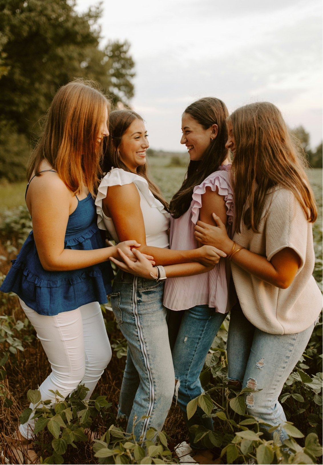 Four women standing in a field, holding hands and smiling at each other.