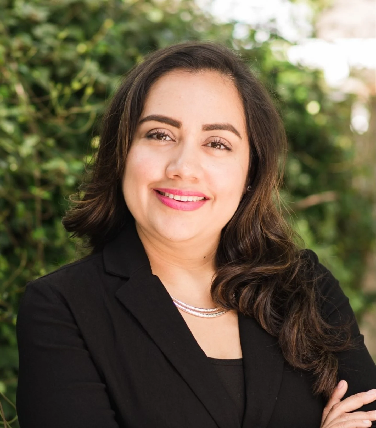 Lizet Orozco, therapist in Katy, TX, wearing a black blazer and smiling, standing outdoors with a background of greenery.