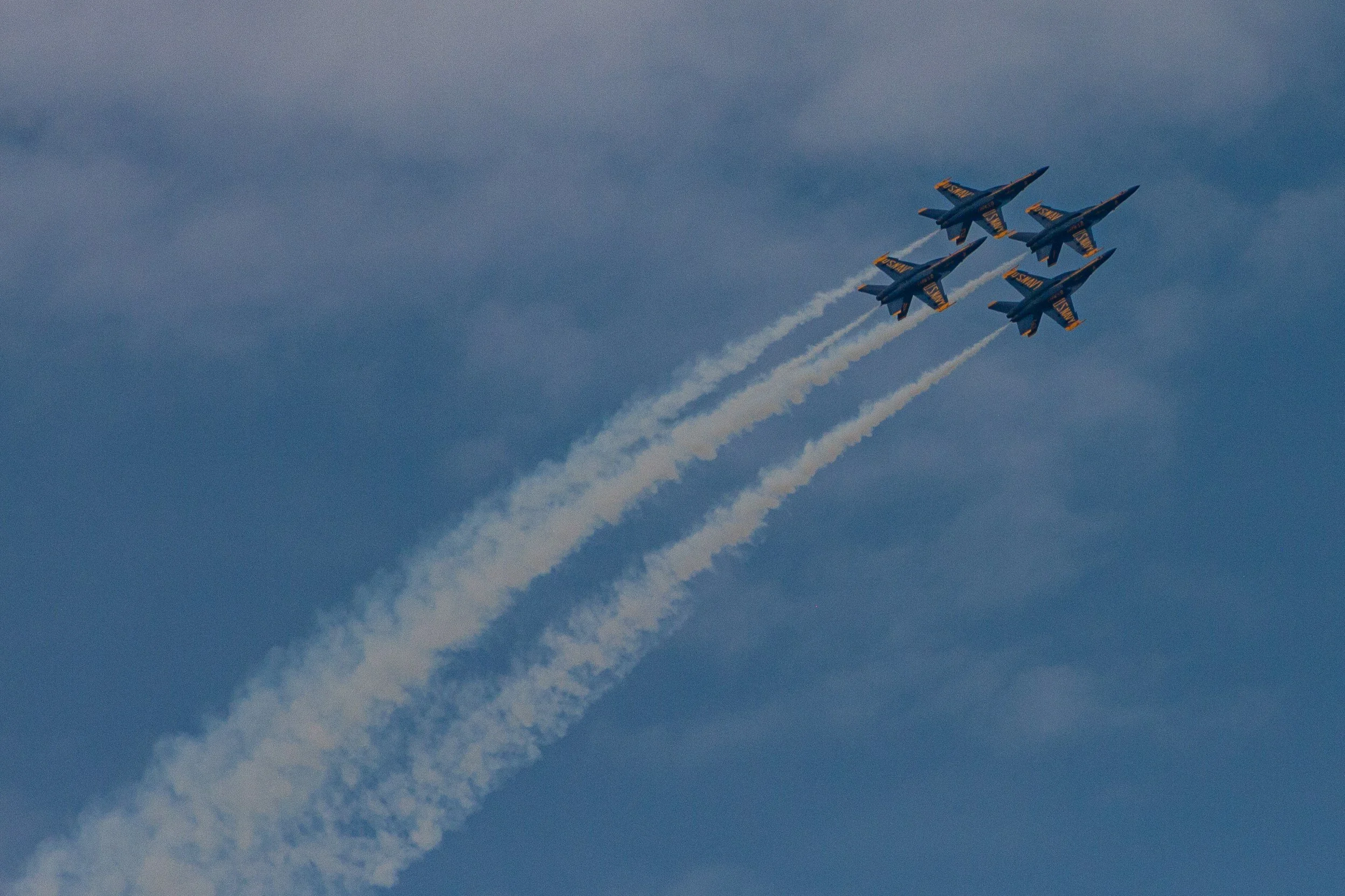 Four aircraft fly together with long white contrails against blue clouds.