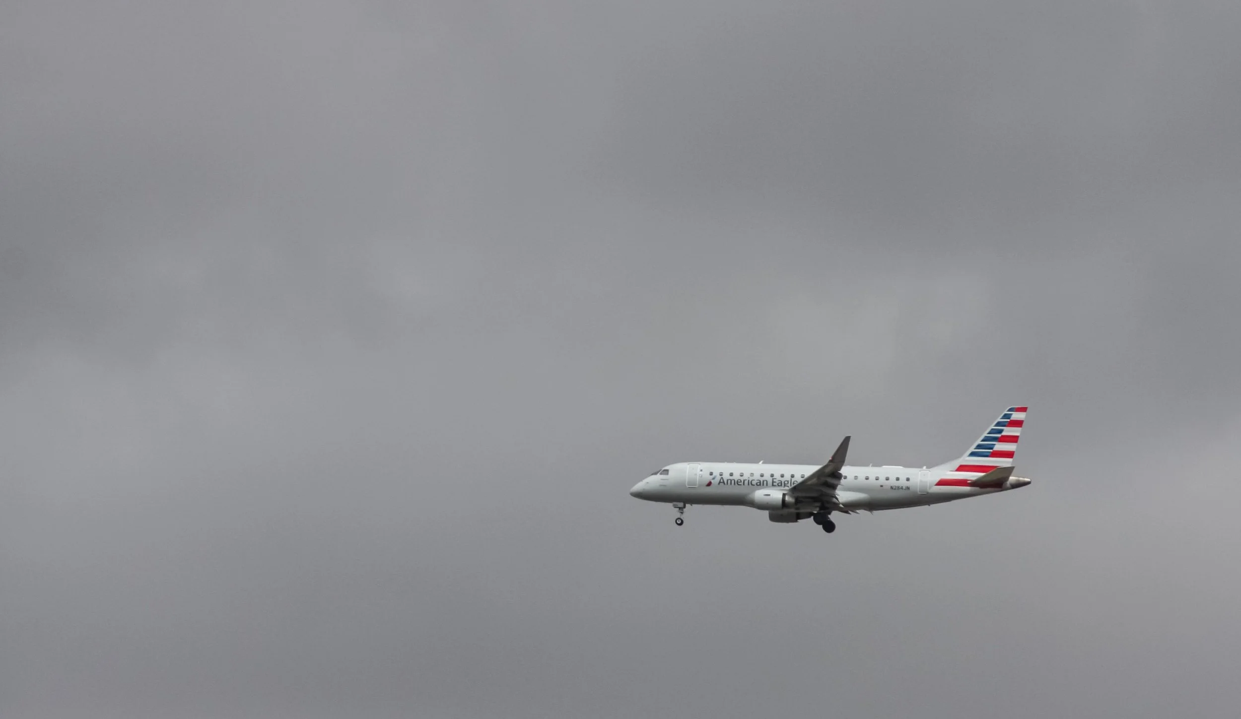 An airliner passes beneath an overcast gray sky.