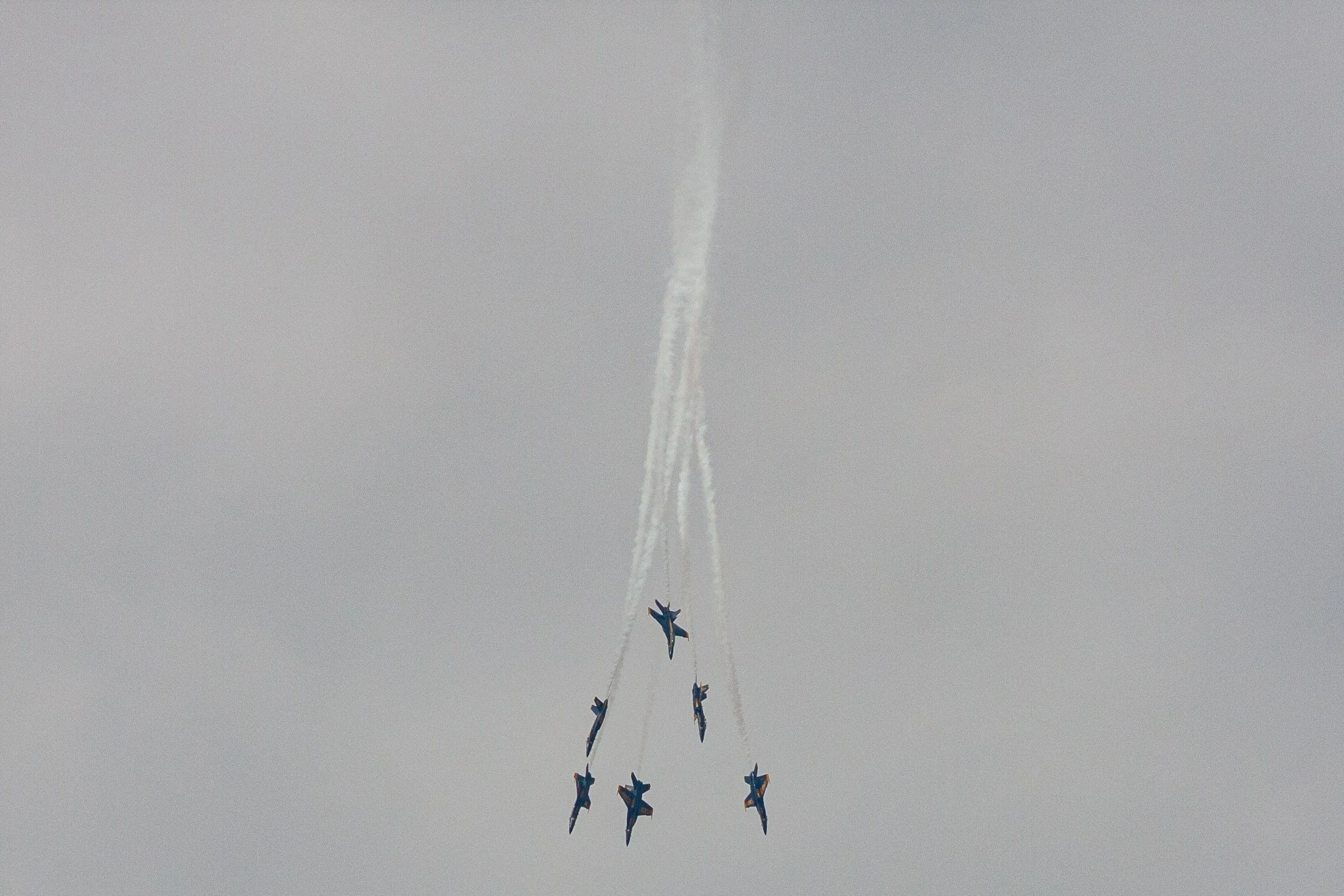 A formation of aircraft climbs beneath long vertical smoke trails.