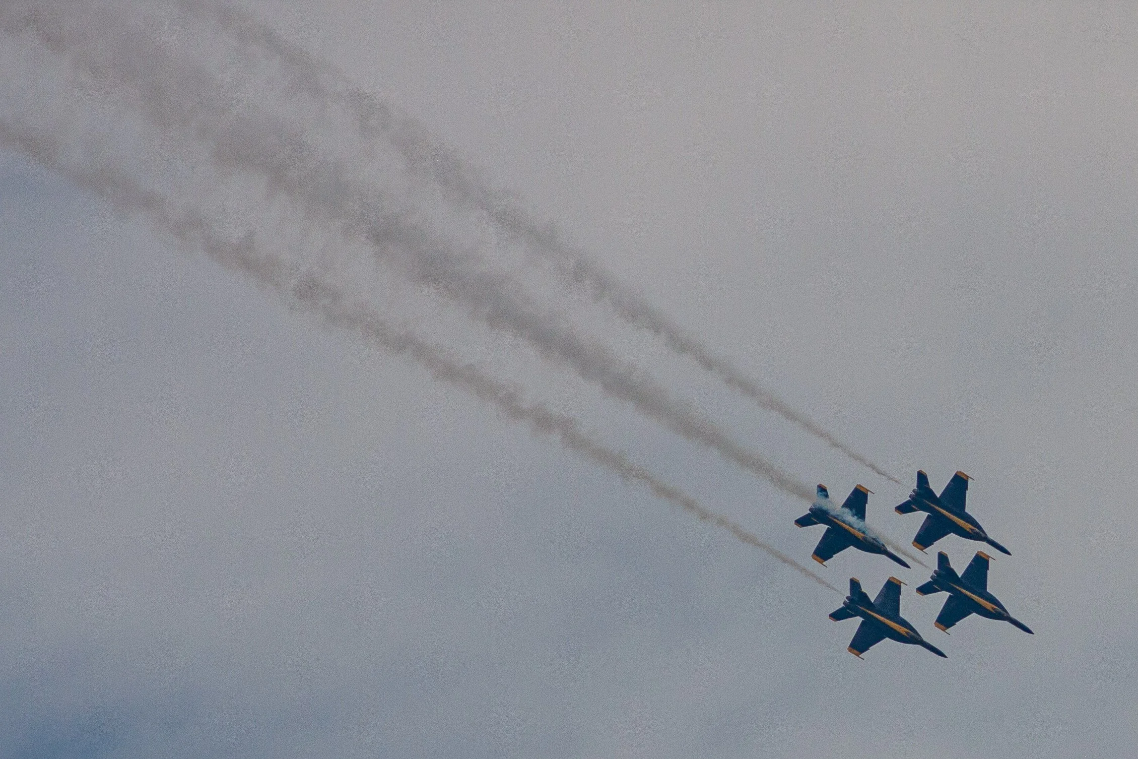 Four Blue Angels aircraft bank together beneath parallel smoke trails.