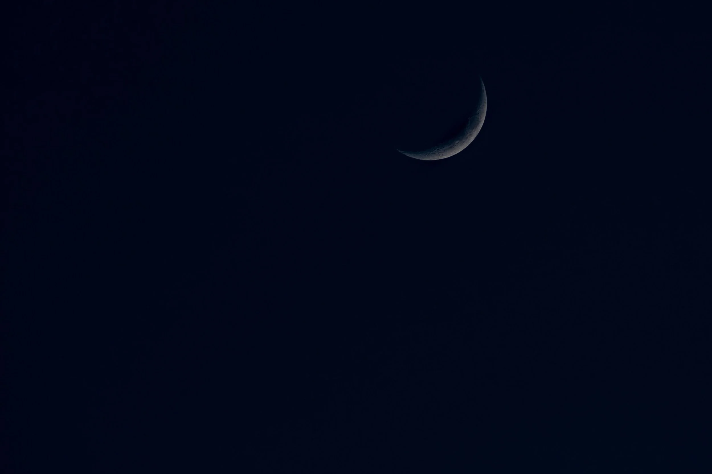 A slender crescent moon curves through a dark blue dusk sky.