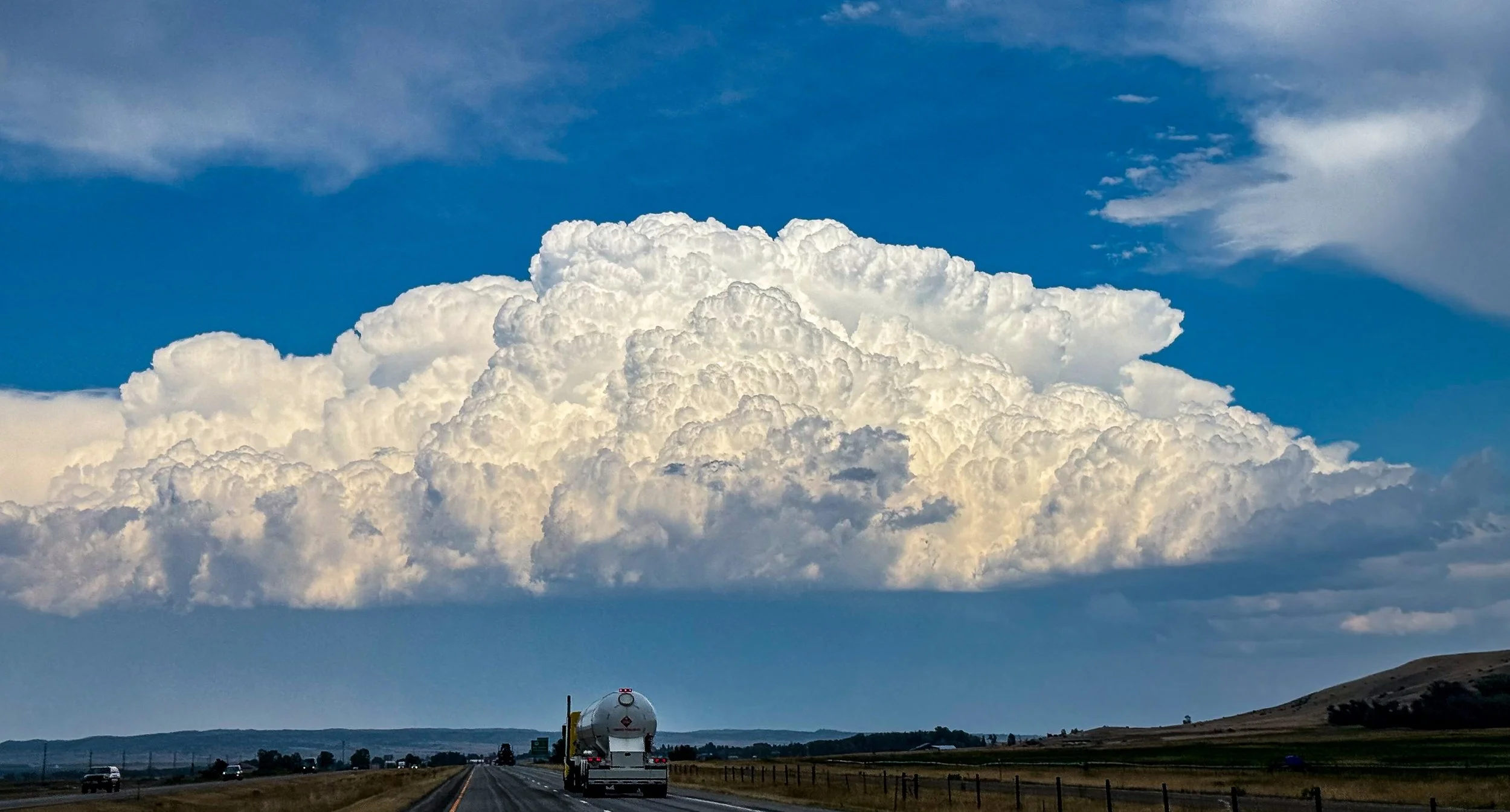 A towering white thunderhead rises above the prairie.