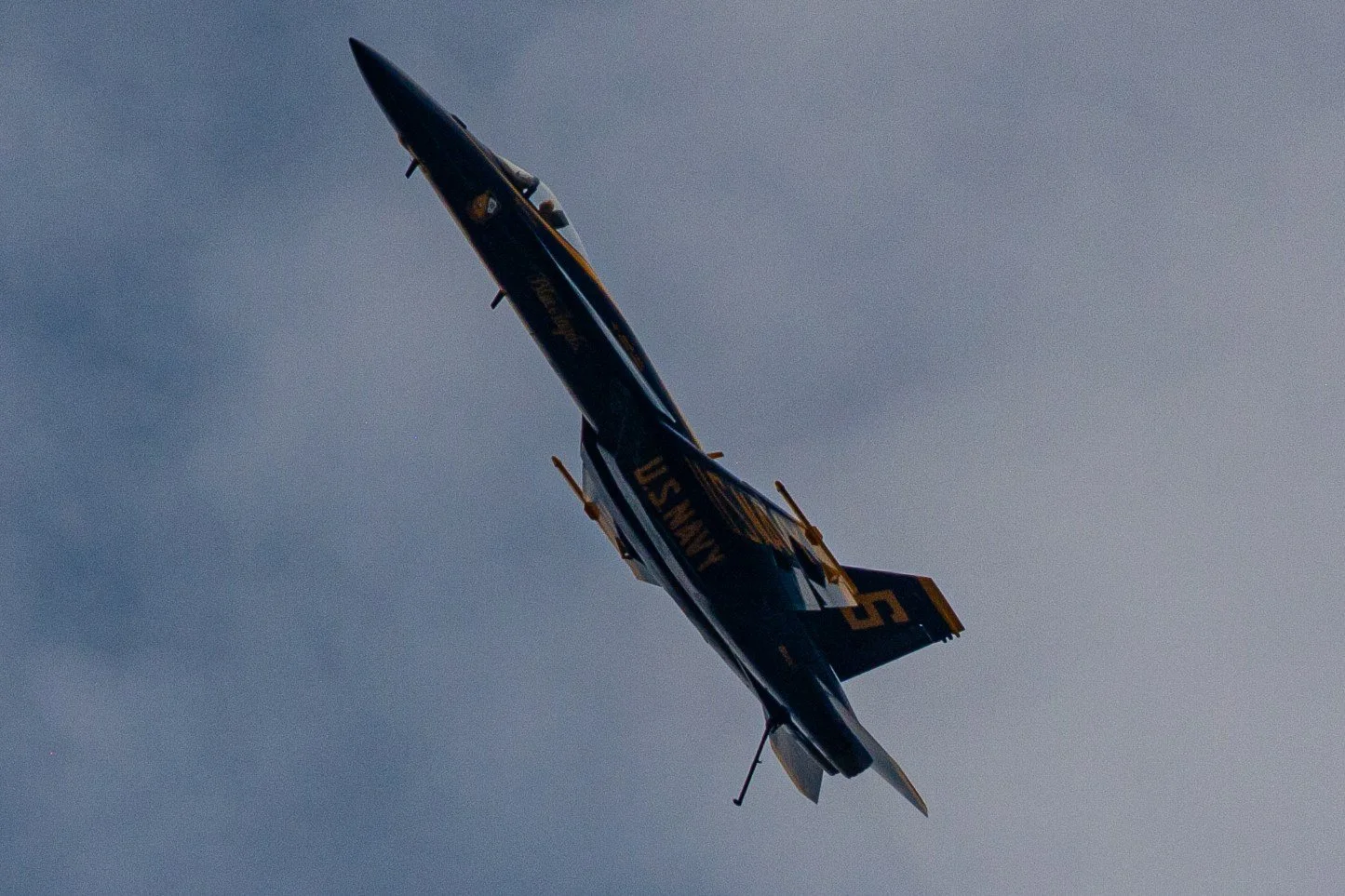A Blue Angels jet banks steeply against a gray sky.