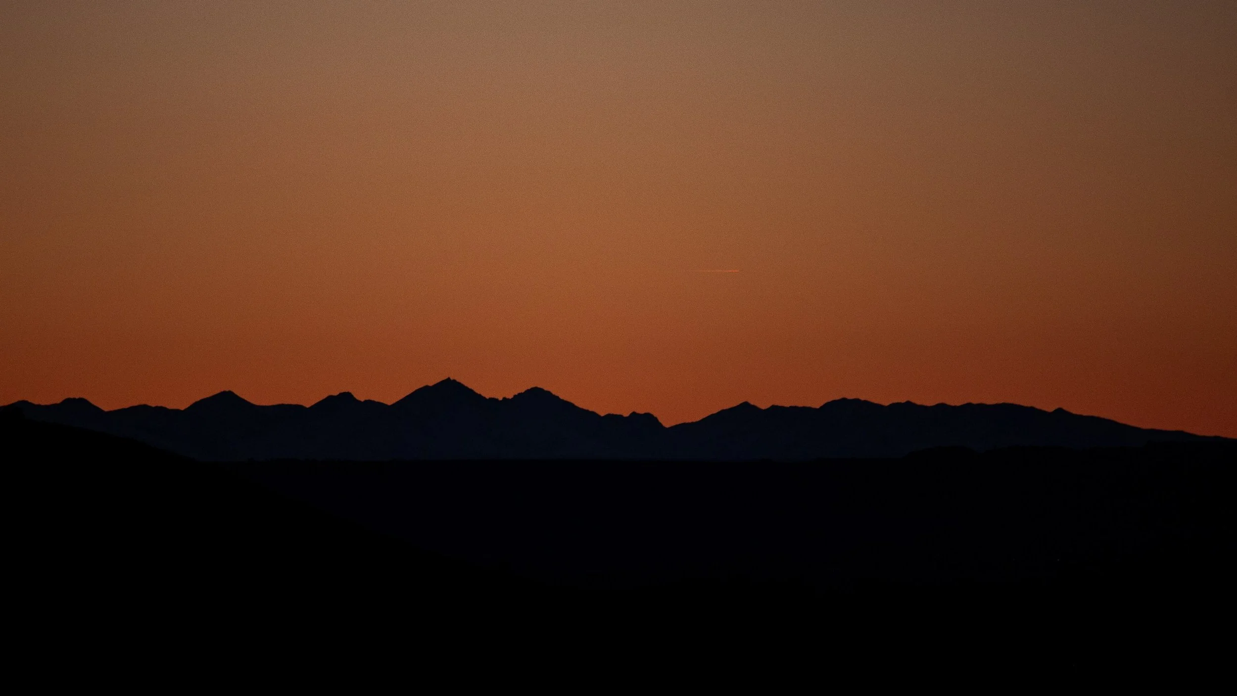 Dark mountain silhouettes meet an orange sunset sky.