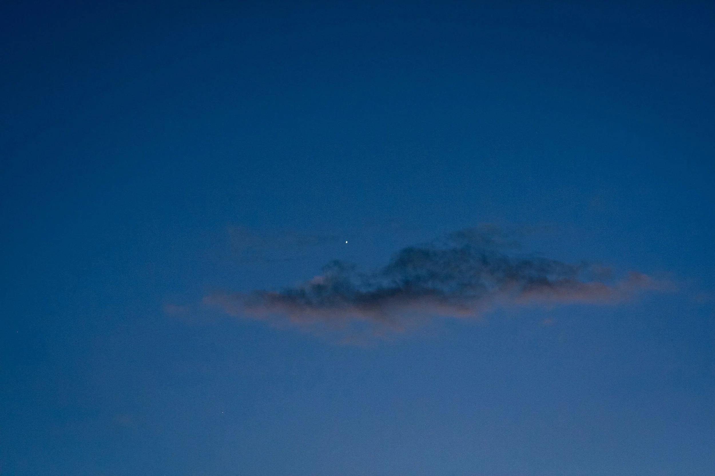 A small cloud catches pink light against a deep blue evening sky.