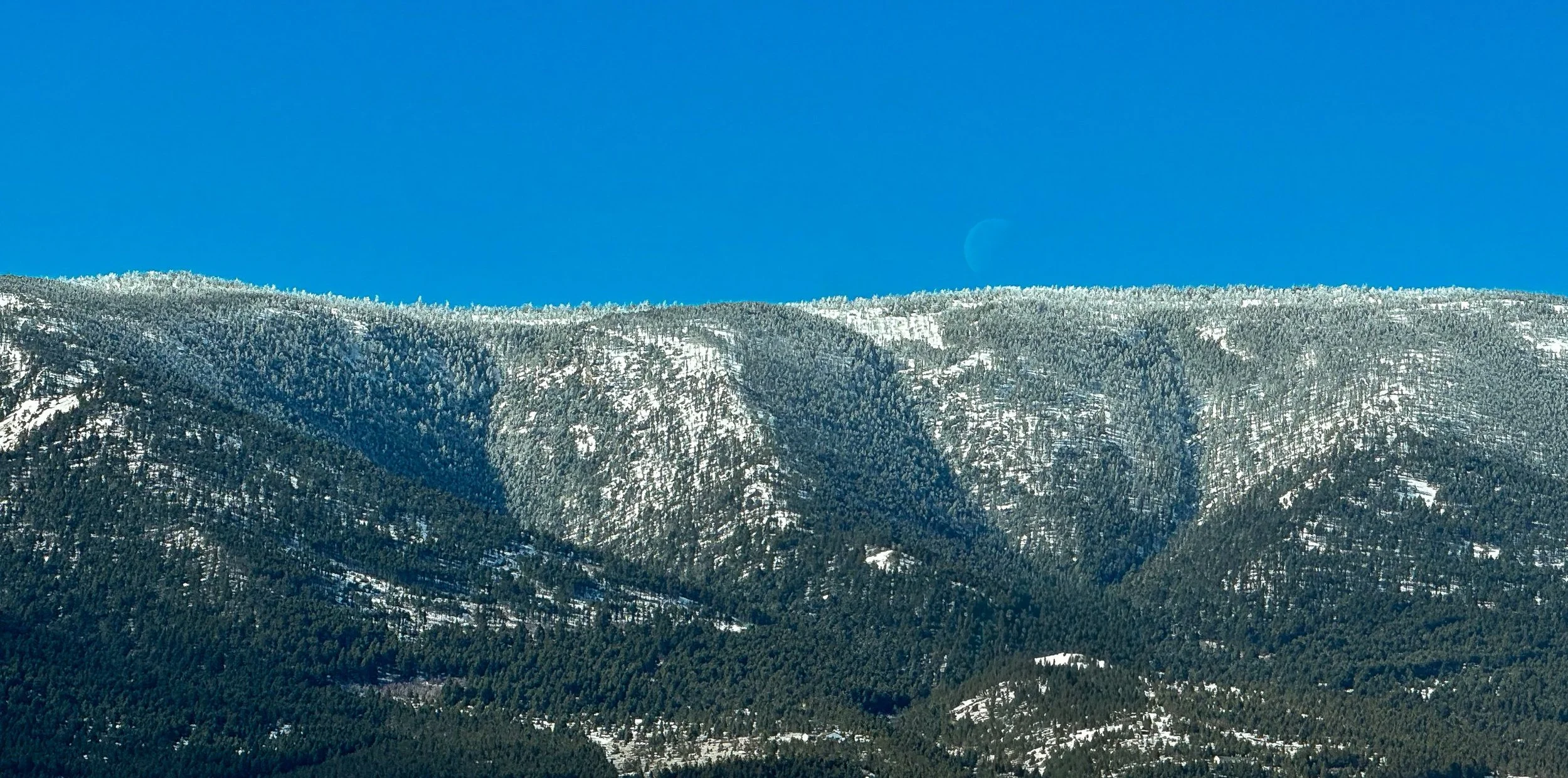 Snow traces the folds of a mountain front beneath a clear blue sky.