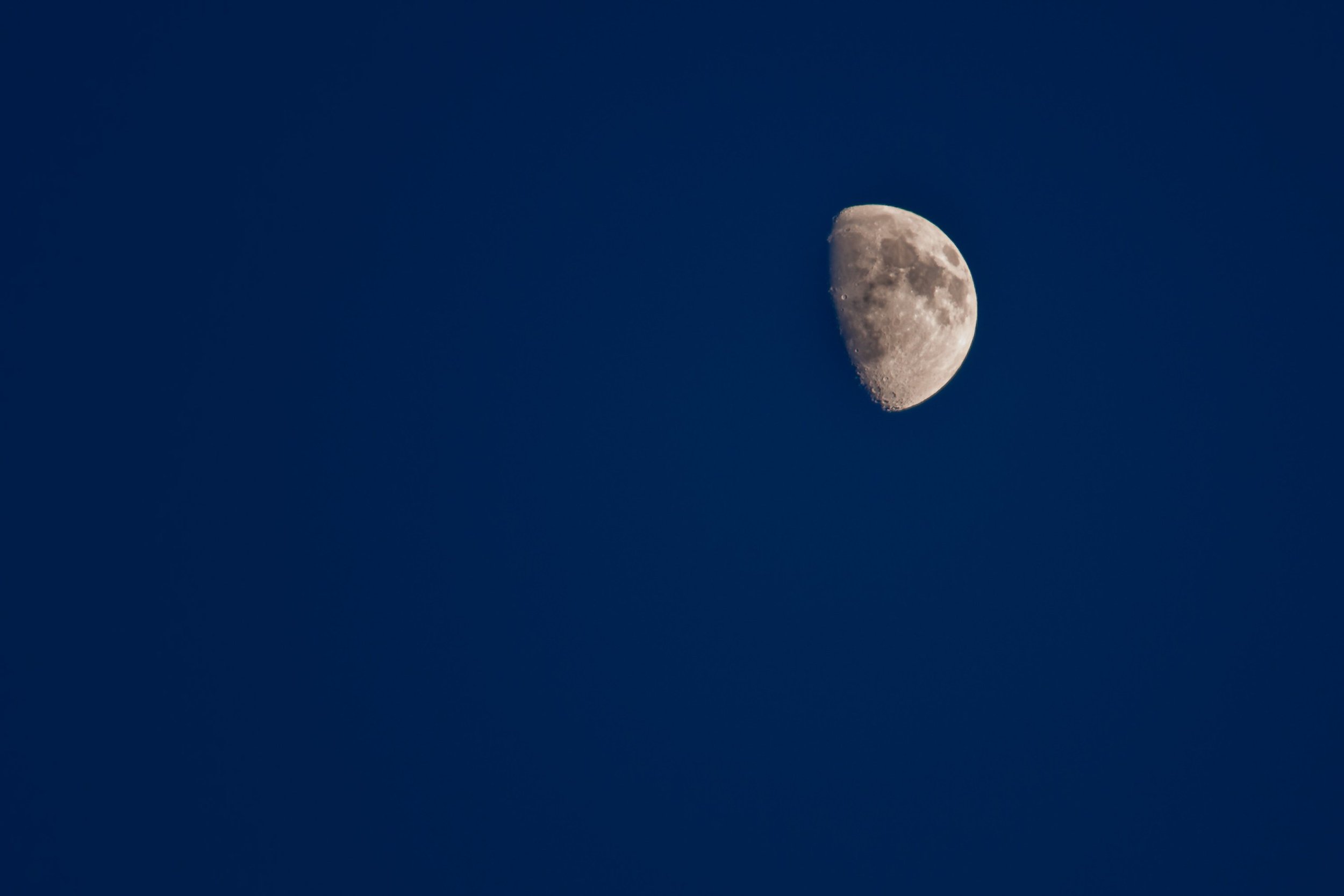 A waxing moon stands out against a clear daytime sky.