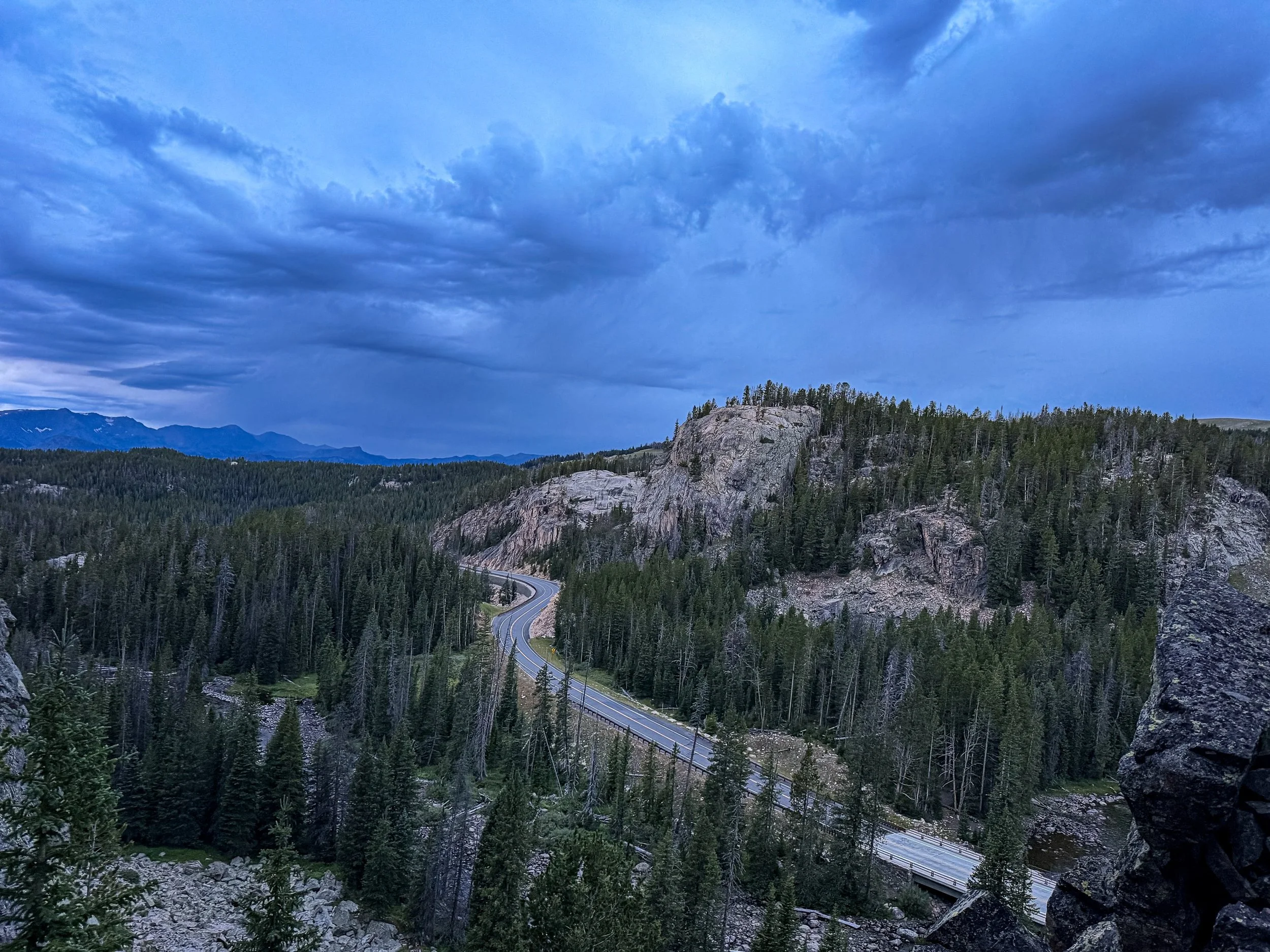 Storm clouds gather above a rocky, forested landscape.