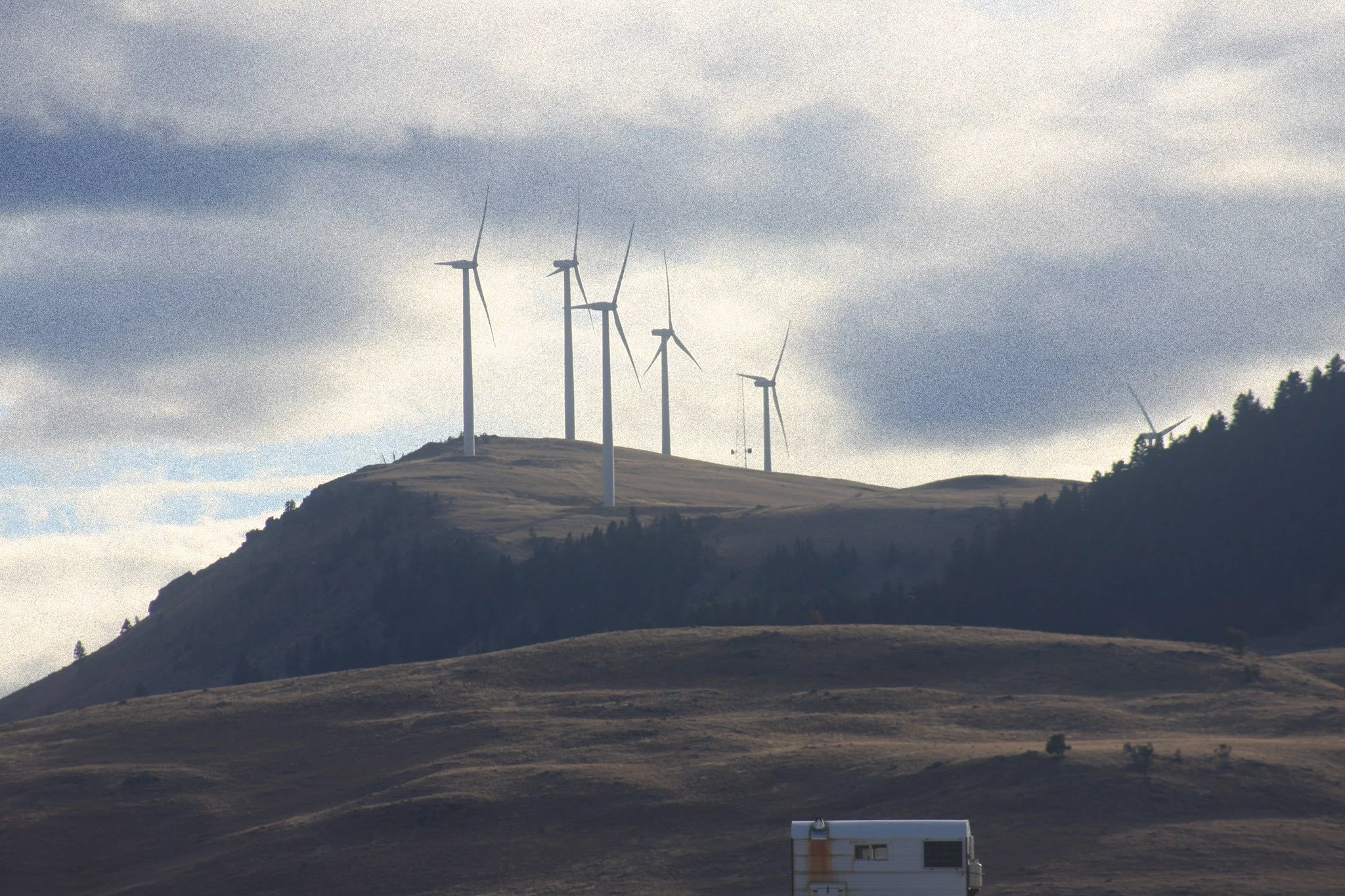 Wind turbines stand along a ridge beneath layered gray clouds.